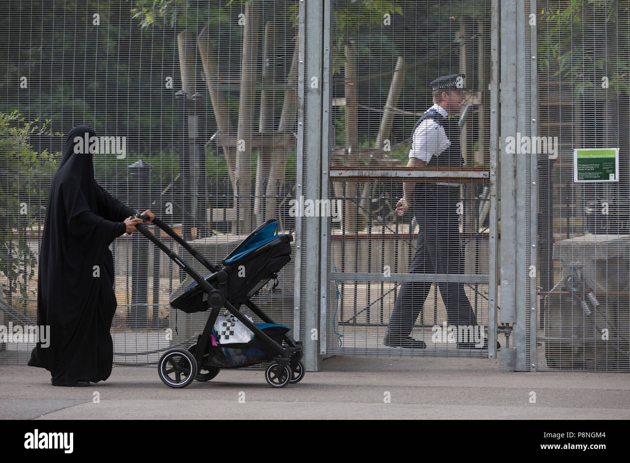 Eine muslimische Frau Spaziergänge Vergangenheit UK Met Polizisten, Guard eine vorübergehende Umzäunung Einkreisung Winfield House, die offizielle Residenz des US-Botschafters beim Besuch des britischen von US-Präsident, Donald Trump, am 12. Juli 2018, im Regent's Park, London, England. Stockfoto