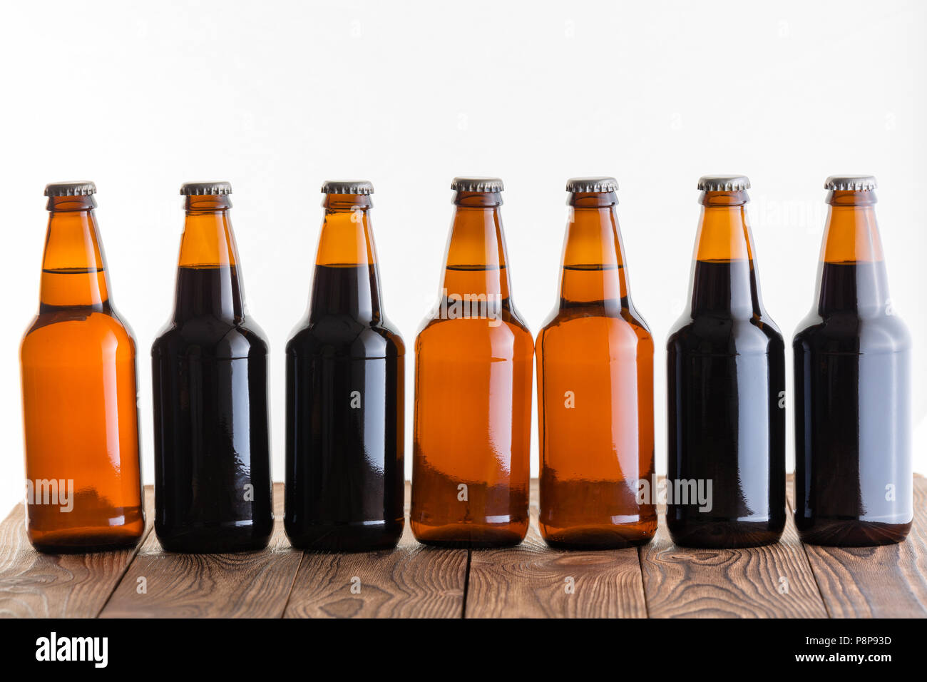 Reihe von Dunkelheit und Licht nicht etikettierten Flaschen mit hausgemachten Handwerk Bier auf einem rustikalen Holztisch vor einem weißen Hintergrund Stockfoto