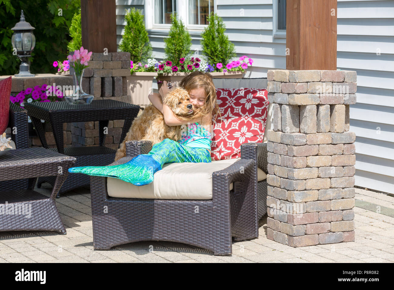 Glückliche junge Mädchen in einer Meerjungfrau Kostüm entspannen auf einer Terrasse Tisch ihr goldenes Cocker Spaniel Welpen umarmen in eine Show der Zuneigung Stockfoto