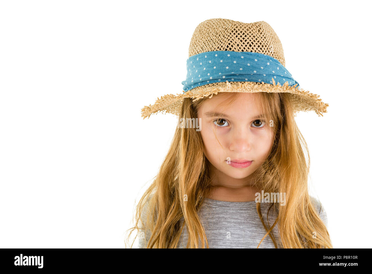 Feierliche dachte, kleinen 6-jährigen Mädchen mit einem trendigen Stroh Sonnenhut versessen auf die Kamera isoliert auf weißem Stockfoto