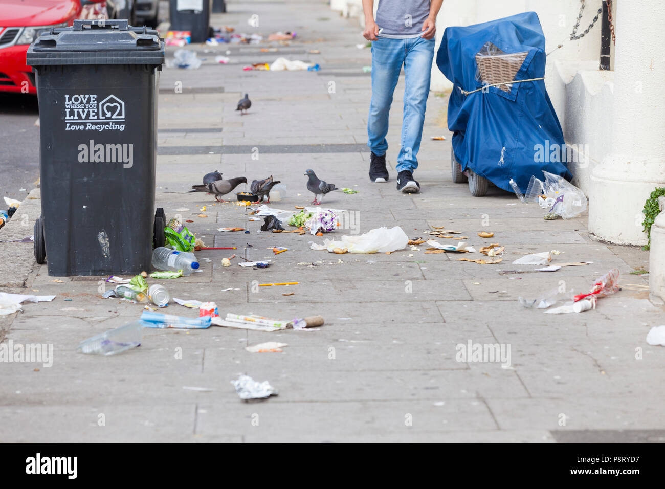 Person zu Fuß vorbei an einem Wurf übersäte Straße mit Tauben Ernte an den Müll auf dem Boden liegend in Hastings, East Sussex, Großbritannien Stockfoto