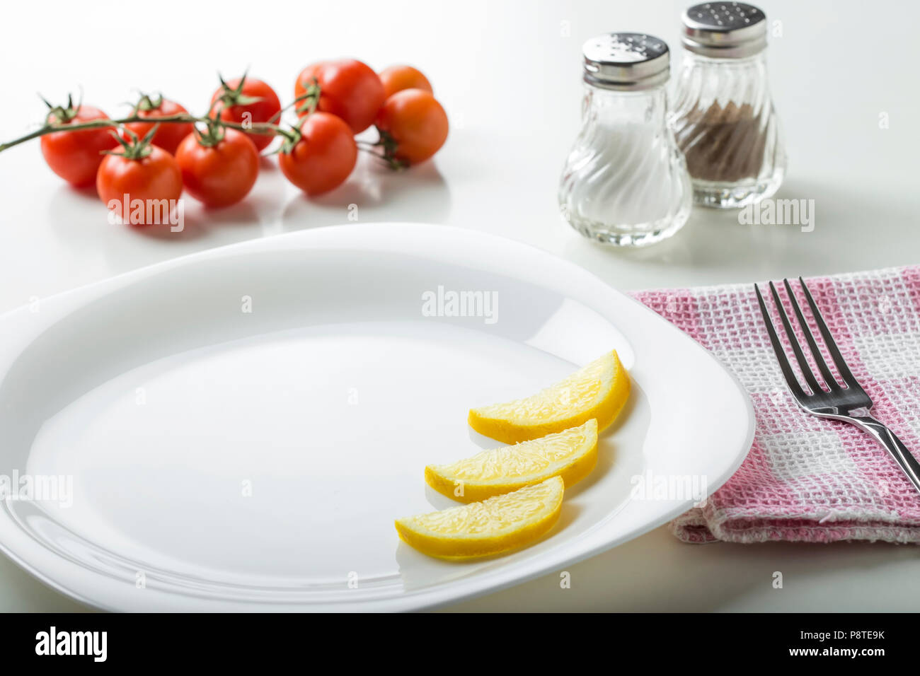 Leeren Teller mit Gabel, Salz- und Pfefferstreuer und Kirschtomaten im Hintergrund Stockfoto