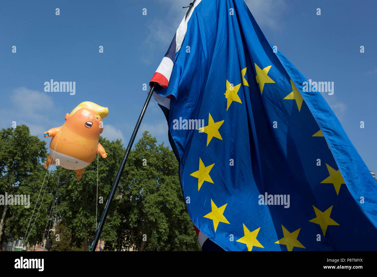 London, Großbritannien. 13. Juli 2018. Die aufblasbaren Ballon namens Baby Trump fliegt über die Fahne der Europäischen Union im Parlament in Westminster, dem Sitz des Parlaments, während der US-Präsident Besuch in Großbritannien. Baby Trump ist eine 20 m hohe orange blimp Darstellung der US-Präsident als wütend, Smartphone auskuppeln Säuglings - und angesichts der besonderen Erlaubnis über das Kapital um Londoner Bürgermeister Sadiq Khan, weil der Protest als künstlerische Natur erscheinen. Es ist das Geistesprodukt des Graphic Designer Matt Bonner. Credit: RichardBaker/Alamy leben Nachrichten Stockfoto