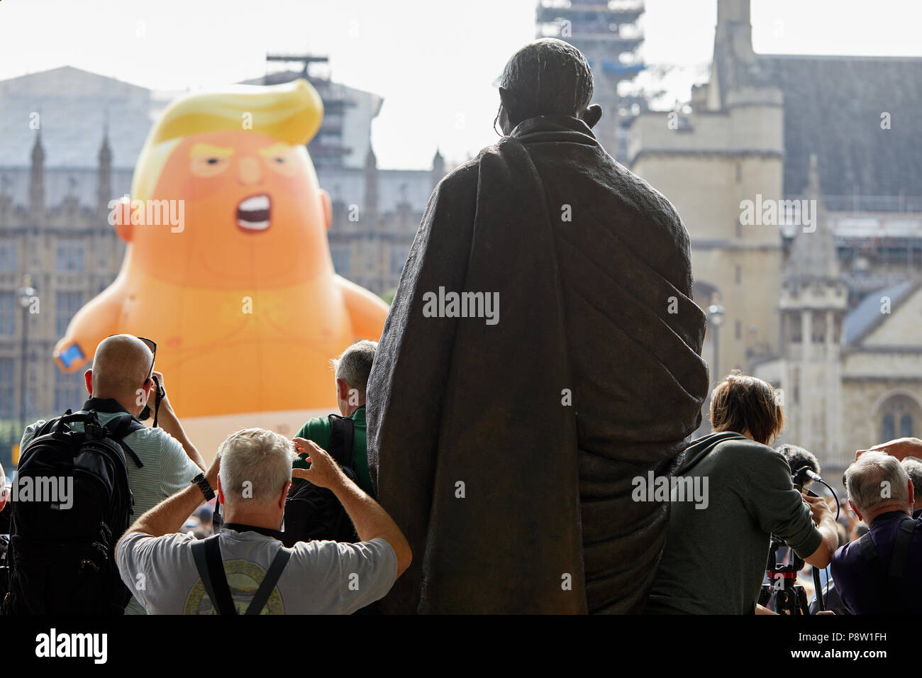 London, Großbritannien, 13. Juli 2018: Fotografen rush Fotos zu machen, als einen riesigen Ballon mocking Donald Trump Ballon gegenüber der Statue von Mahatma Gandhi in Parliament Square angehoben ist. Stockfoto