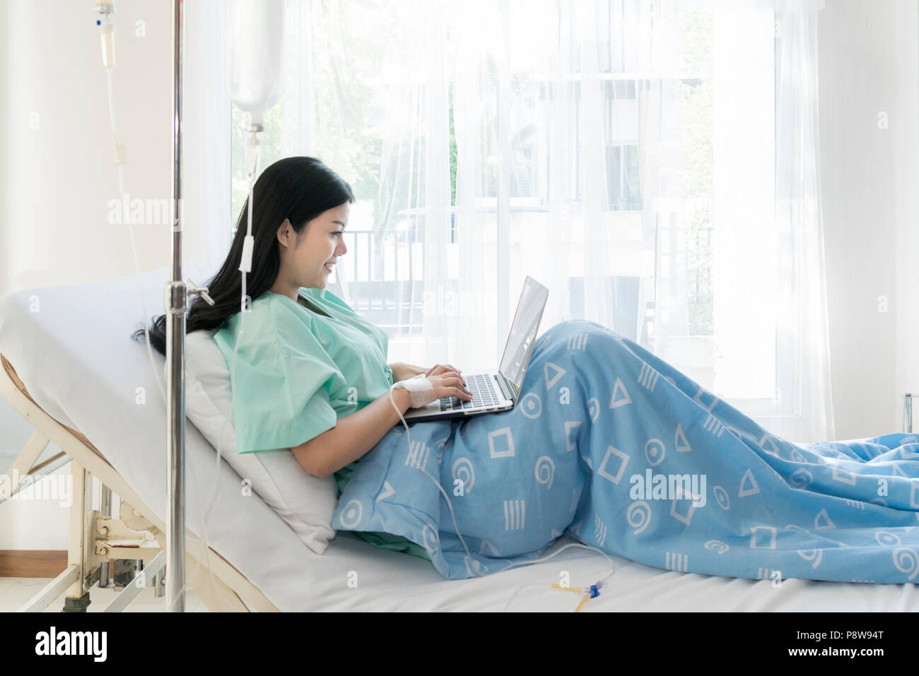 Asiatische Frau kranke Patient in einem Krankenhaus Bett liegend mit einem Laptop für entspannen, wenn Sie die Wiederherstellung für Kranke im Krankenhaus. Stockfoto