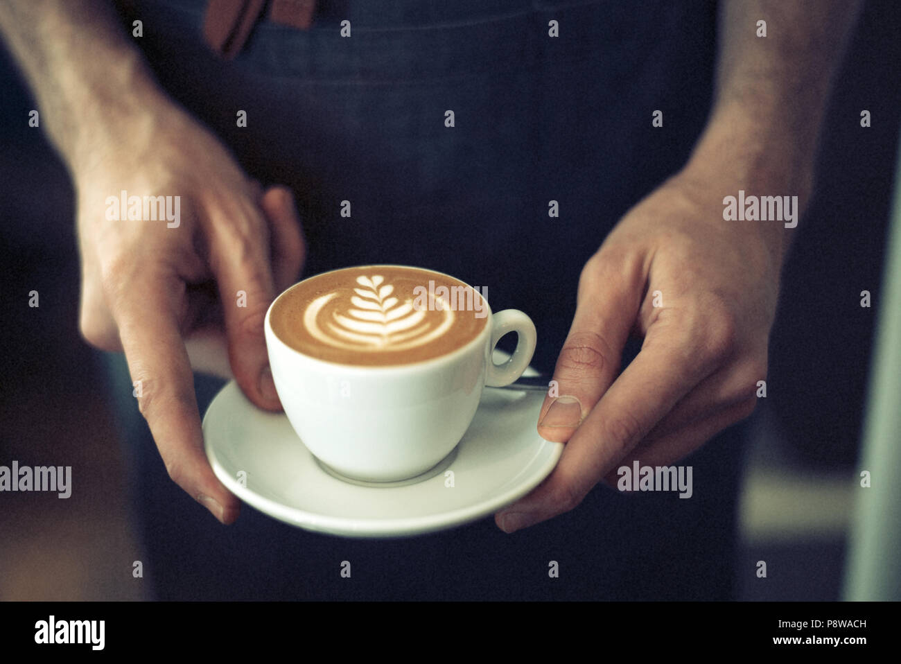 Barista serviert eine schöne flache Weiß mit Latte Art, mit den Händen in der Nähe Stockfoto