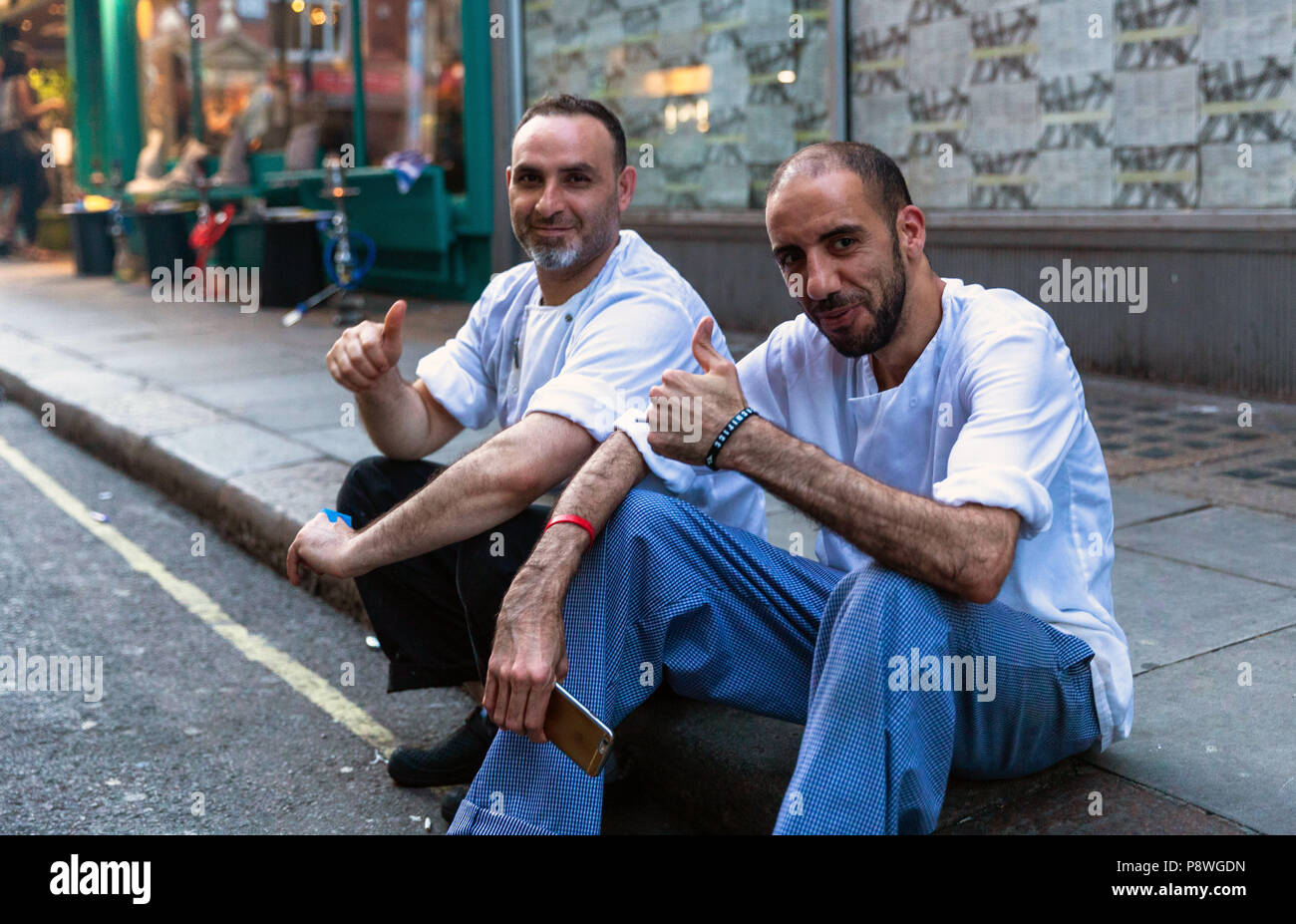 Porträt von zwei männlichen Köchen, die Pause zusammen, sitzen auf dem Bürgersteig, London, England, Großbritannien. Stockfoto