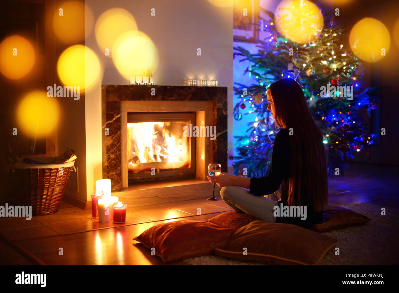 Frau mit einem Drink am Kamin in der gemütlichen dunklen Wohnzimmer am Heiligabend Stockfoto
