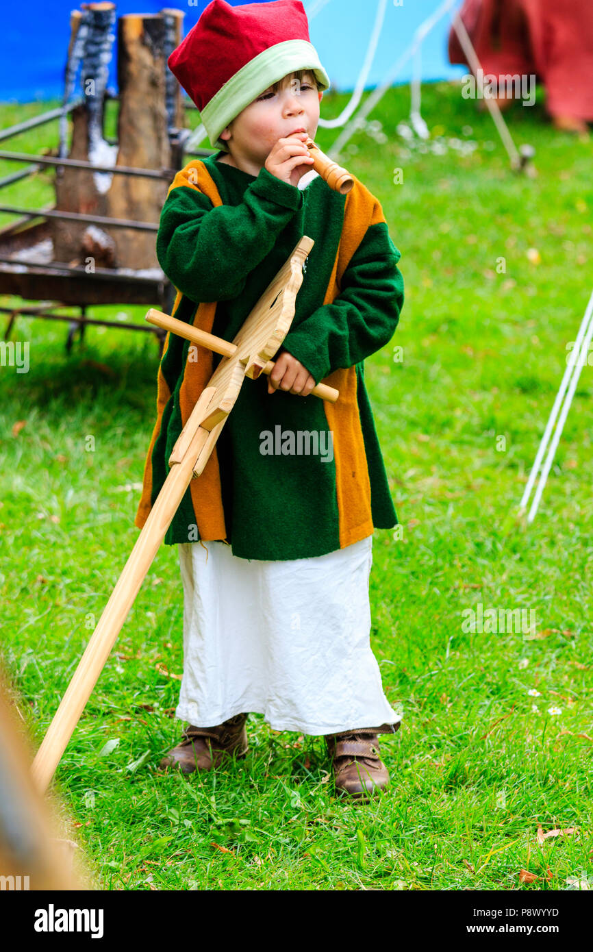 Kind, Junge, 3-4 Jahre alt, im mittelalterlichen Kostüm während lebendige Geschichte reenactment Event. Holding Holz- hobby horse und spielen kleine mini Flöte. Stockfoto