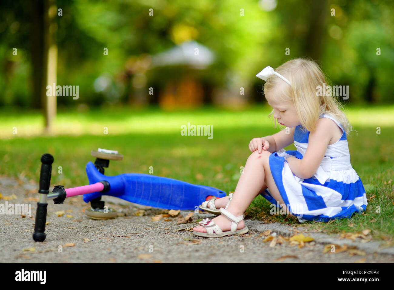 Kleines Mädchen auf dem Boden sitzend, nachdem Sie fiel, während das reiten Ihr scooter am Sommer, Park Stockfoto