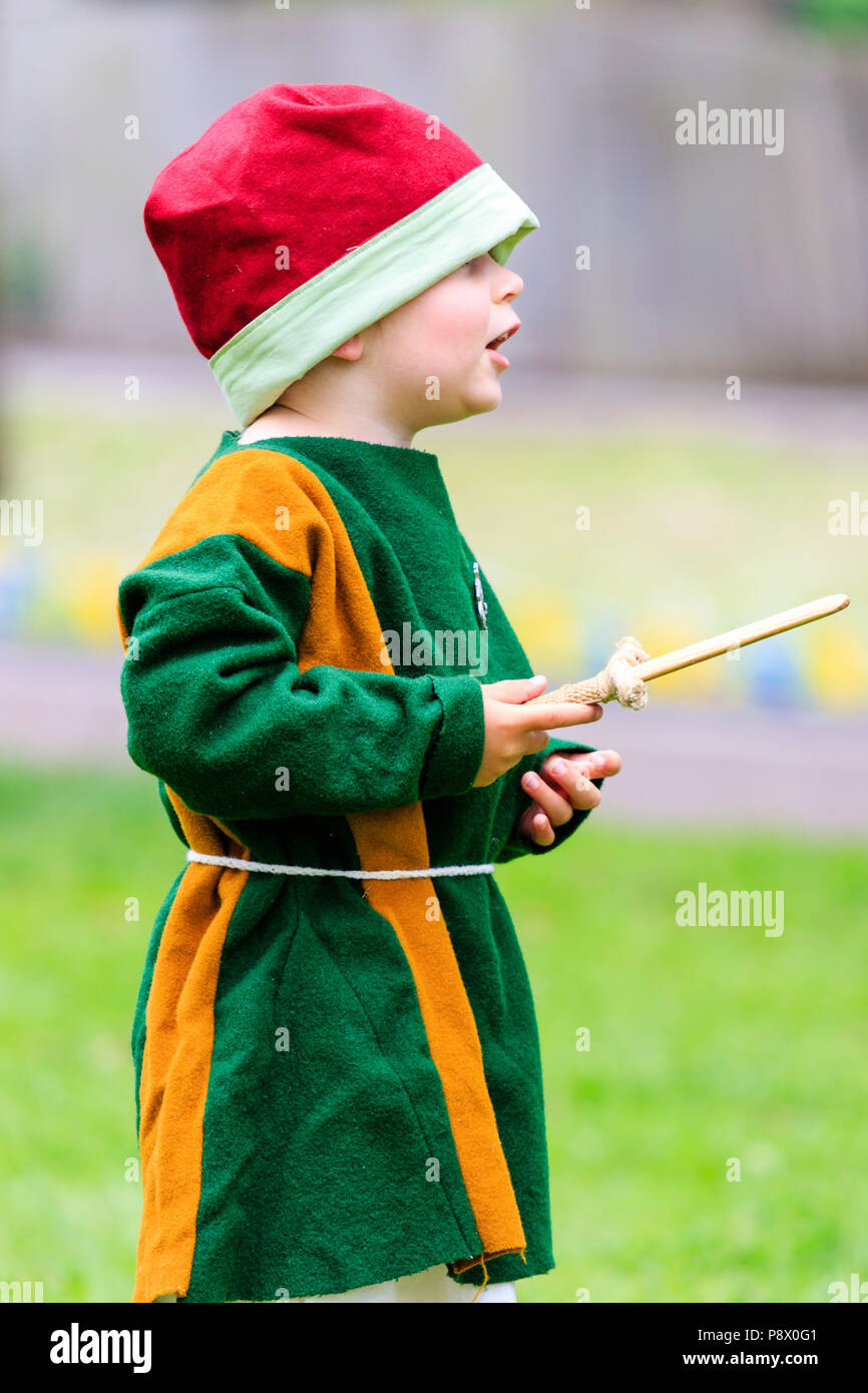 Kind, Junge, 3-4 Jahre alt, im mittelalterlichen Kostüm während lebendige Geschichte reenactment Event. Holding Holz- Dolch, beim Stehen draußen auf Gras. Stockfoto