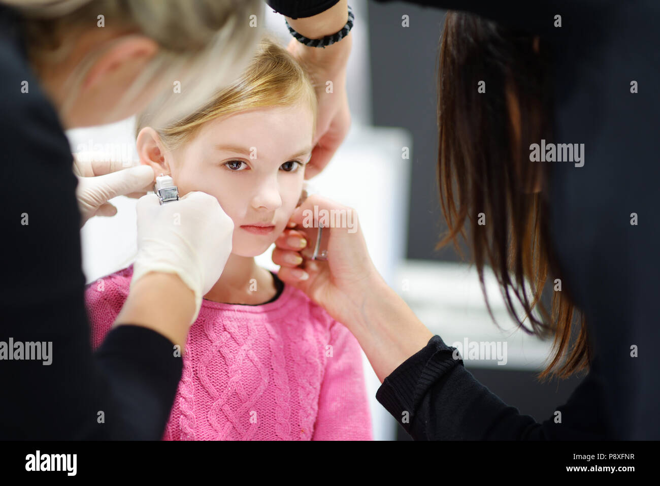 Adorable kleine Mädchen in Ohr Piercing Prozess mit Sonderausstattung im Beauty Center durch medizinische Mitarbeiter Stockfoto
