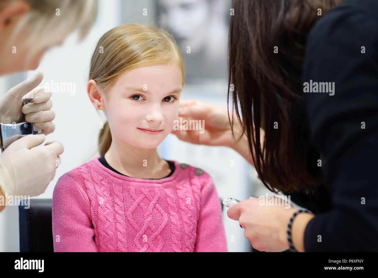 Adorable kleine Mädchen in Ohr Piercing Prozess mit Sonderausstattung im Beauty Center durch medizinische Mitarbeiter Stockfoto