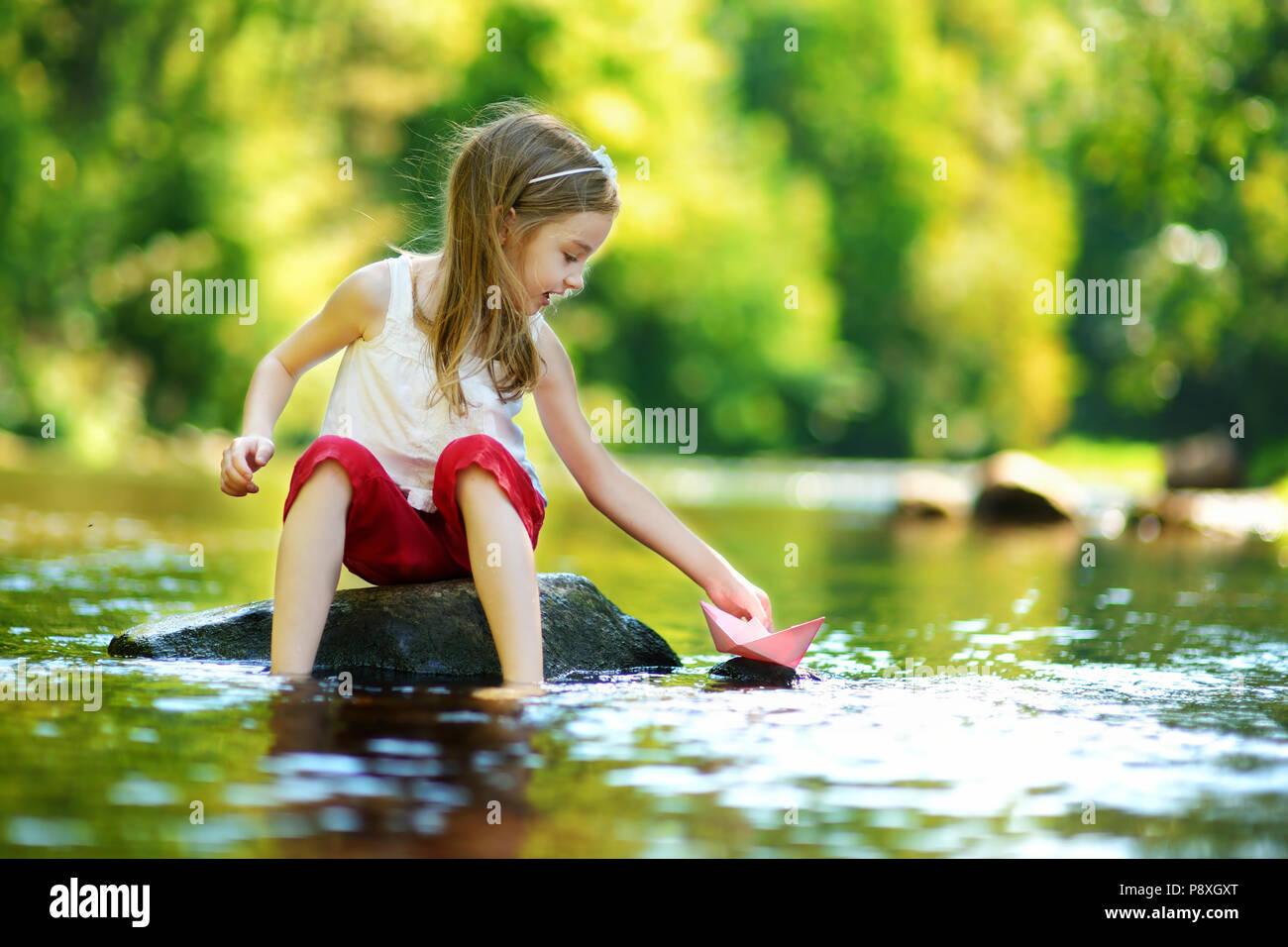 Süße kleine Mädchen spielen mit Papier Boot durch einen Fluss an warmen und sonnigen Sommer Tag Stockfoto
