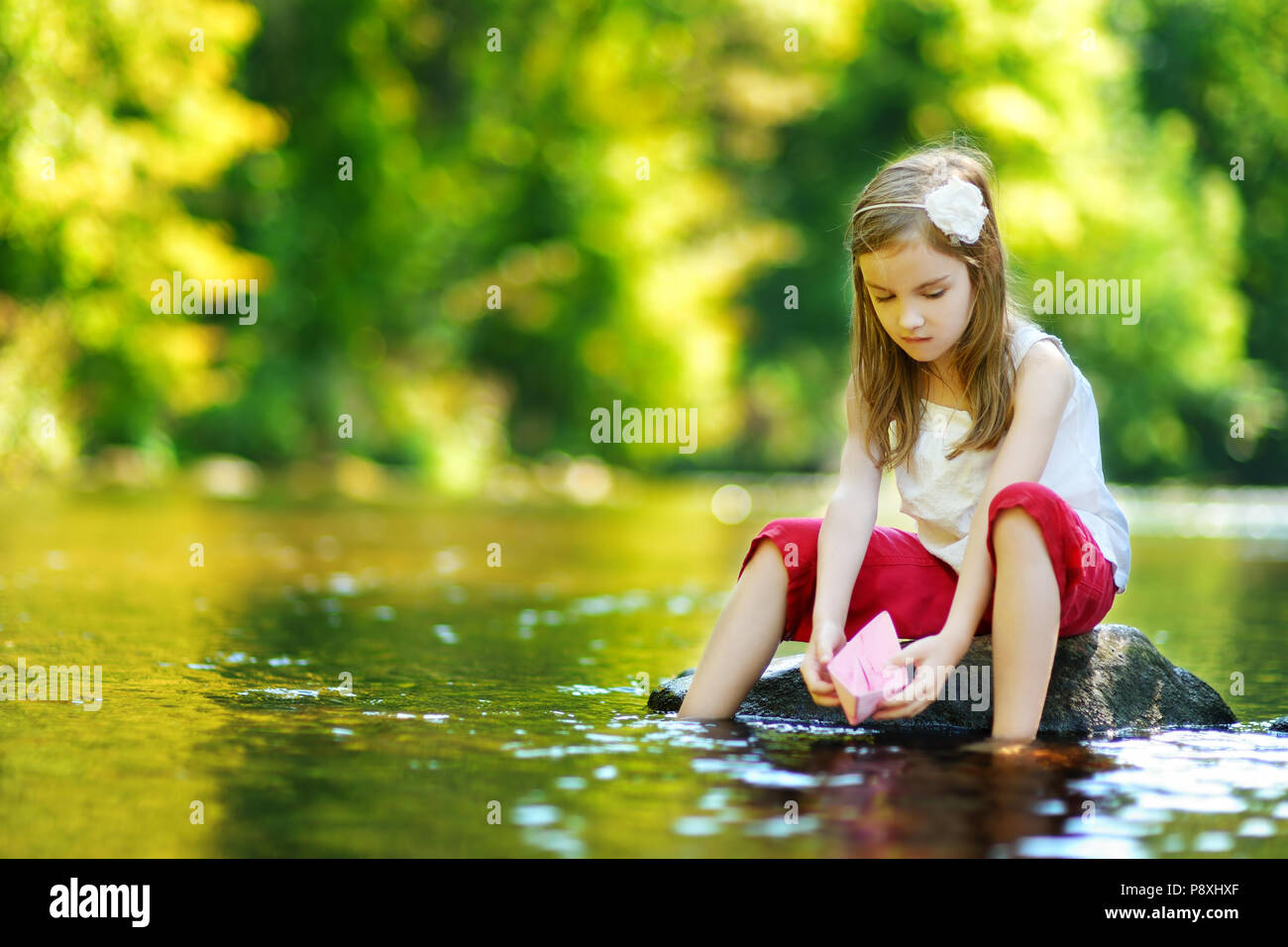Süße kleine Mädchen spielen mit Papier Boot durch einen Fluss an warmen und sonnigen Sommer Tag Stockfoto