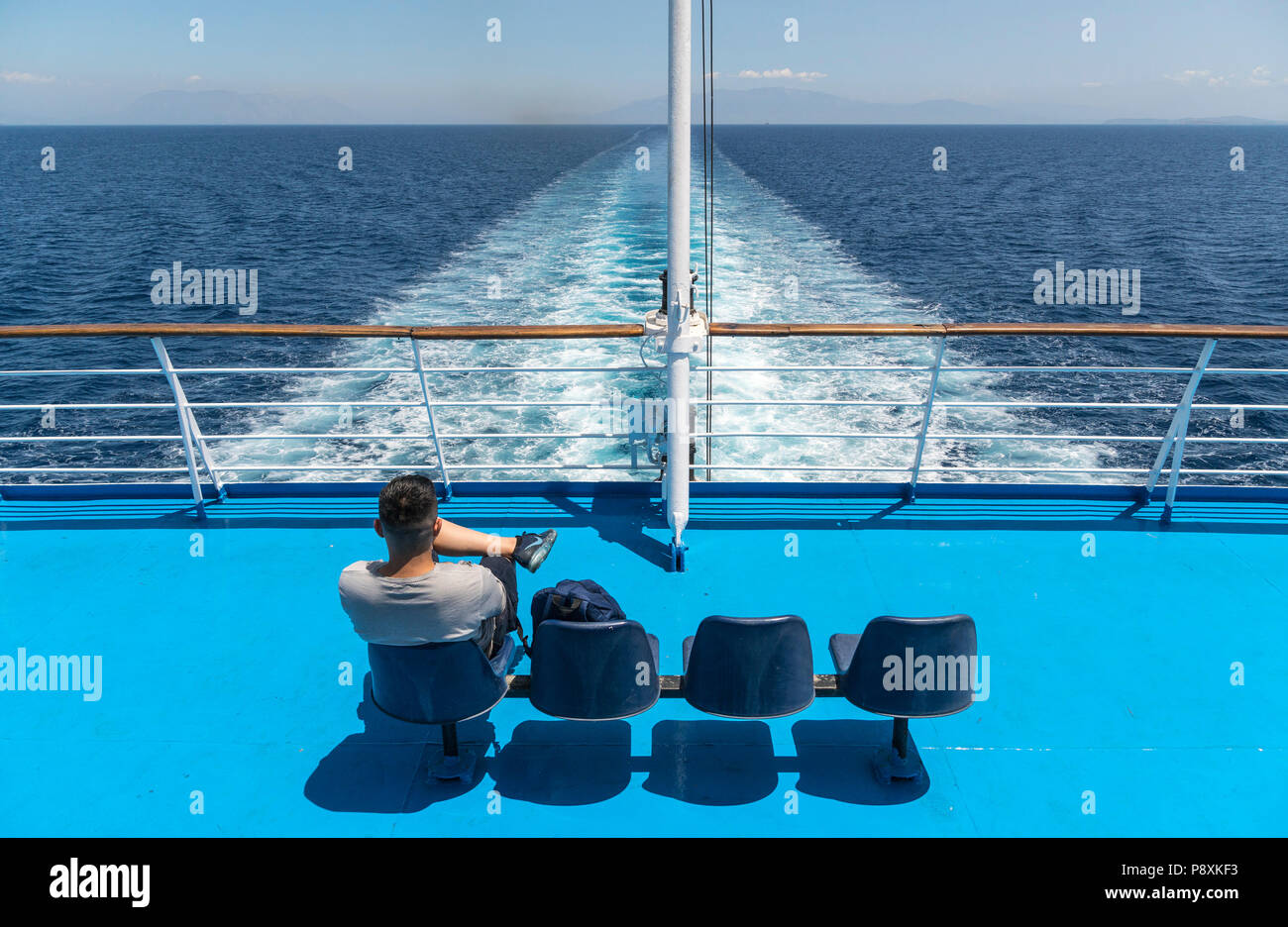 Beifahrer auf dem Stern einer griechischen Fähre beobachten, der Schiff und Fliehendes Land. Stockfoto