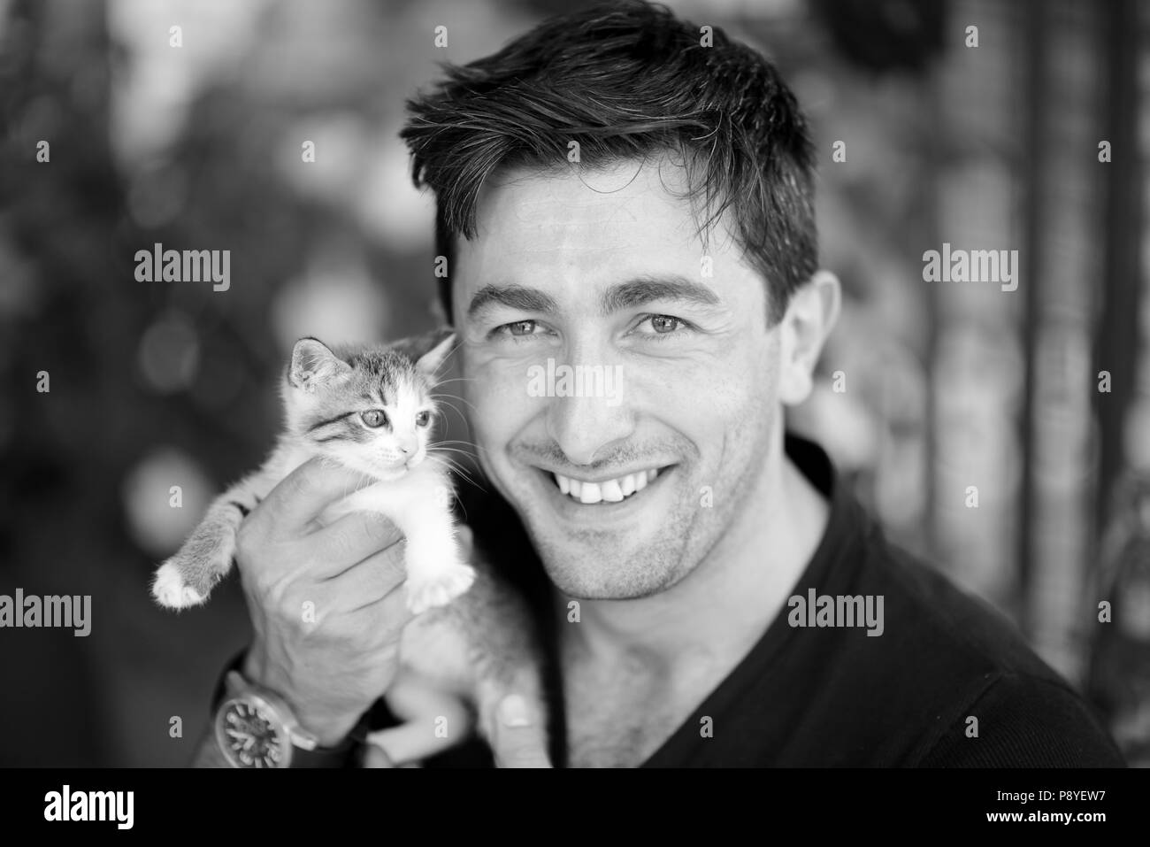 Junger Mann, der ein Kätzchen in den Händen hält und ein Schwarz-Weiß-Foto lächelt Stockfoto