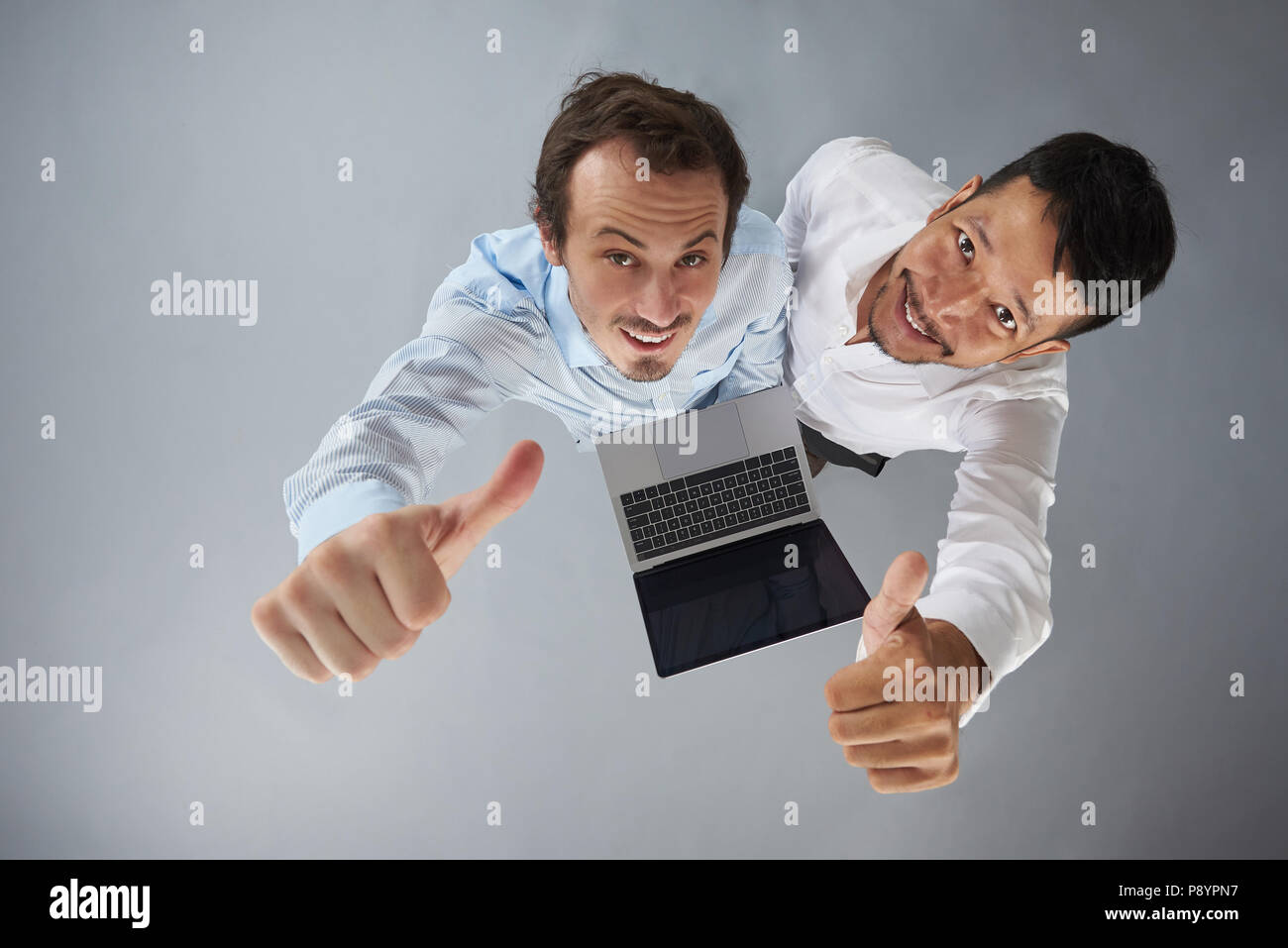 Zwei Mann mit Laptop mit Daumen hoch auf grauem Hintergrund über der oberen Ansicht isoliert Stockfoto