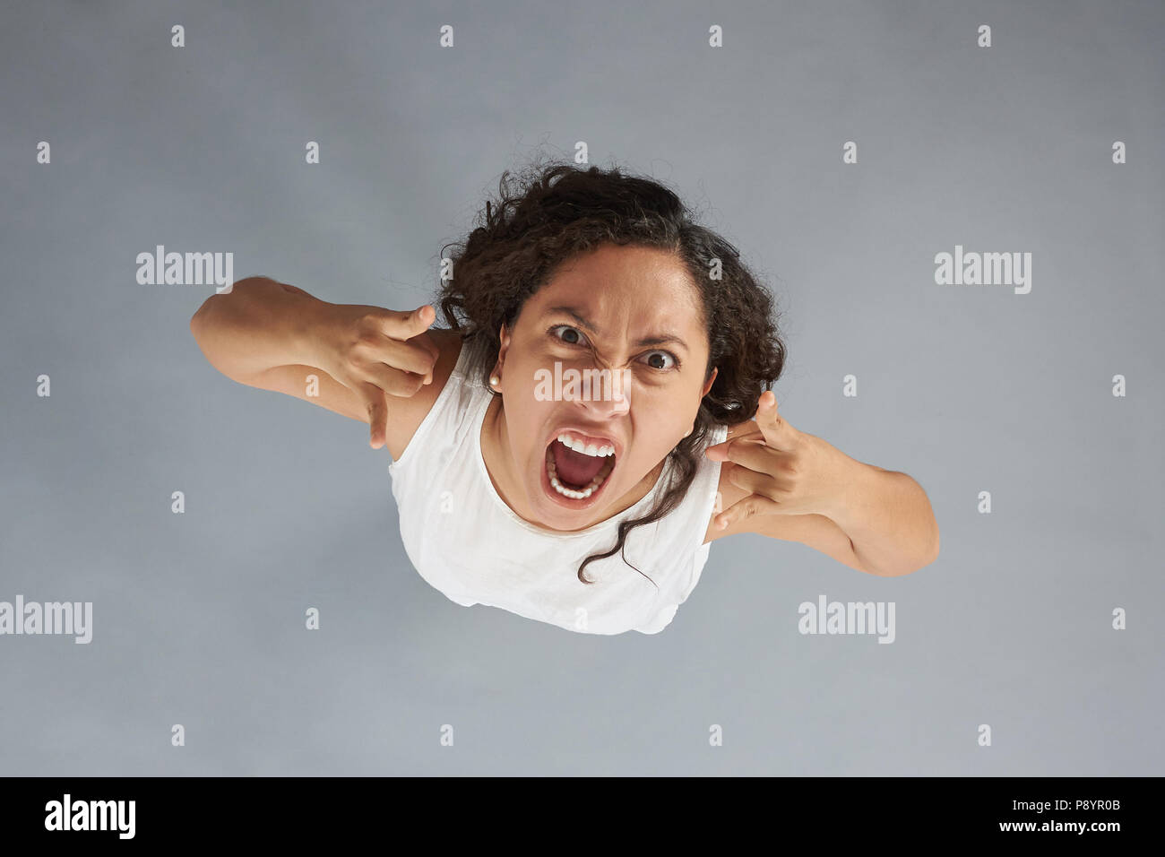 Verrückte junge Frau mit verärgerten Ausdruck auf grauem Hintergrund über der oberen Ansicht isoliert Stockfoto