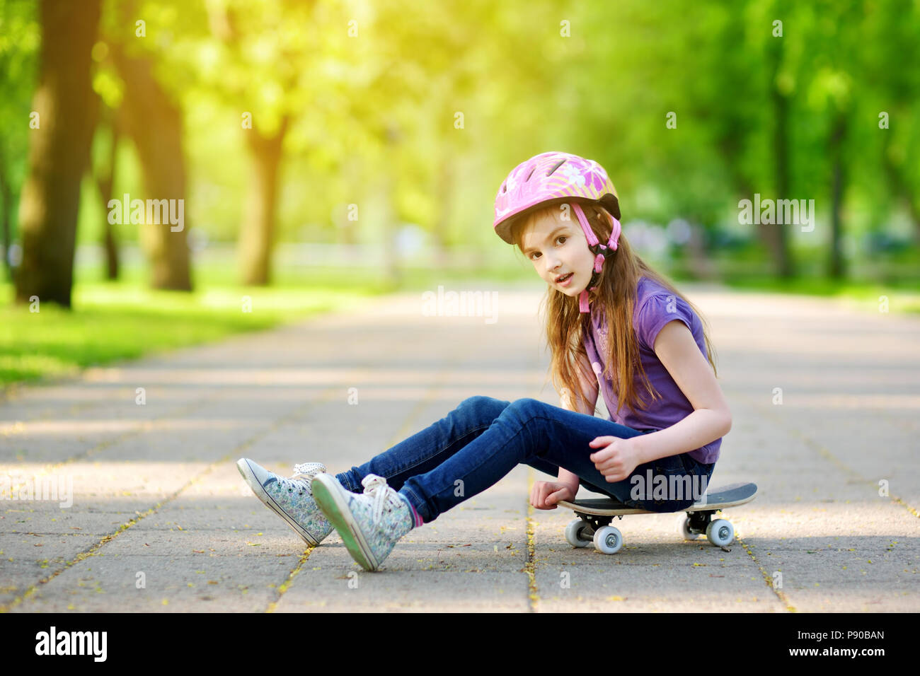 Niedliche kleine preteen Mädchen mit Helm sitzt auf einem Skateboard in schönen Sommerpark Stockfoto