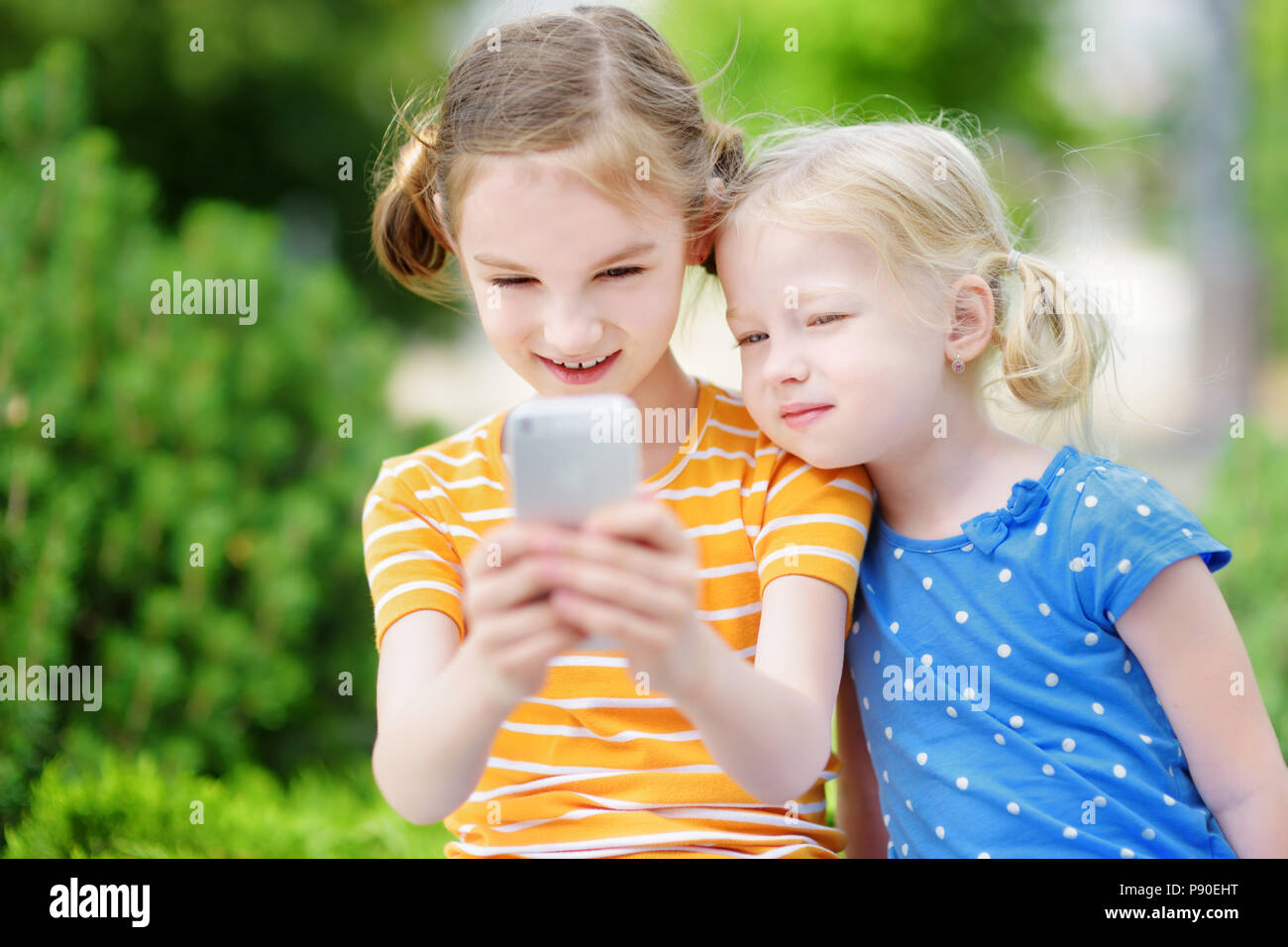 Zwei süße kleine Schwestern spielen Im freien Spiel auf ihren Smartphones. Kinder fangen virtuellen Pocket Monster. Moderne süchtig multiplayer Lage Stockfoto