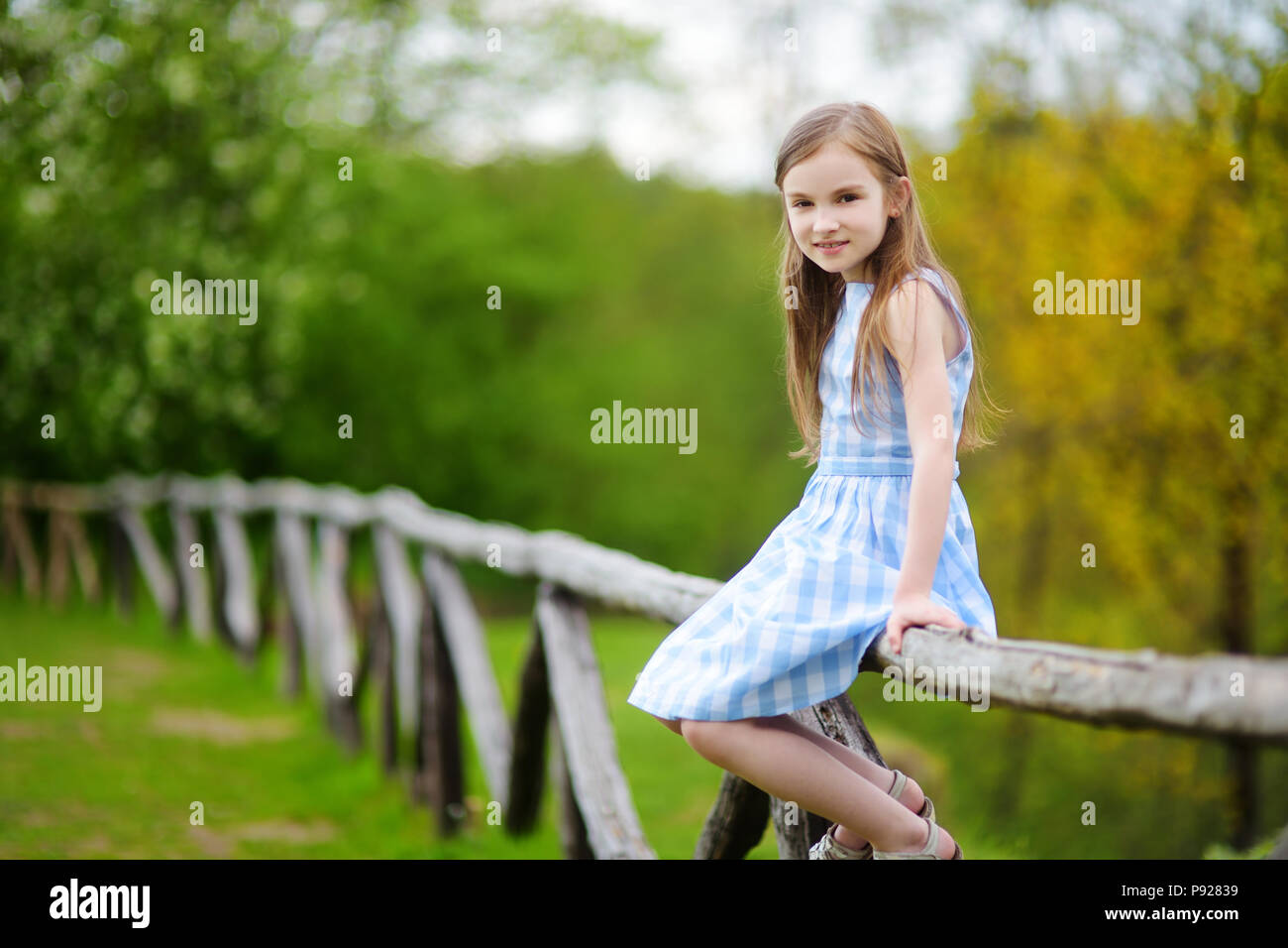 Adorable kleine Mädchen sitzen auf einem hölzernen Zaun auf schönen Frühlingstag. Kind Spaß im Freien im Sommer. Stockfoto
