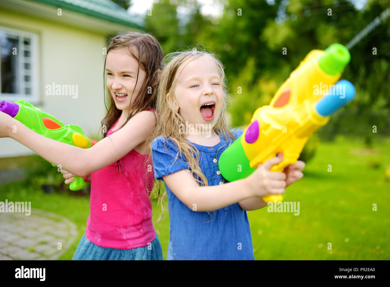 Adorable kleine Mädchen spielen mit Wasser Gewehren auf heißen Sommertag. Süße Kinder Spaß mit Wasser im Freien. Lustige Spiele für Kinder. Stockfoto