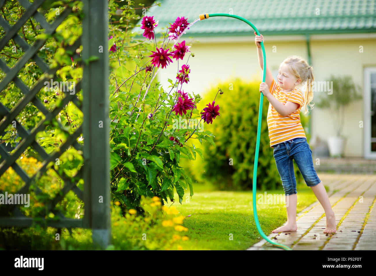 Süße kleine Mädchen Blumen gießen im Garten am Sommer, der Tag. Kind mit Gartenschlauch an einem sonnigen Tag. Mummys little Helper. Stockfoto