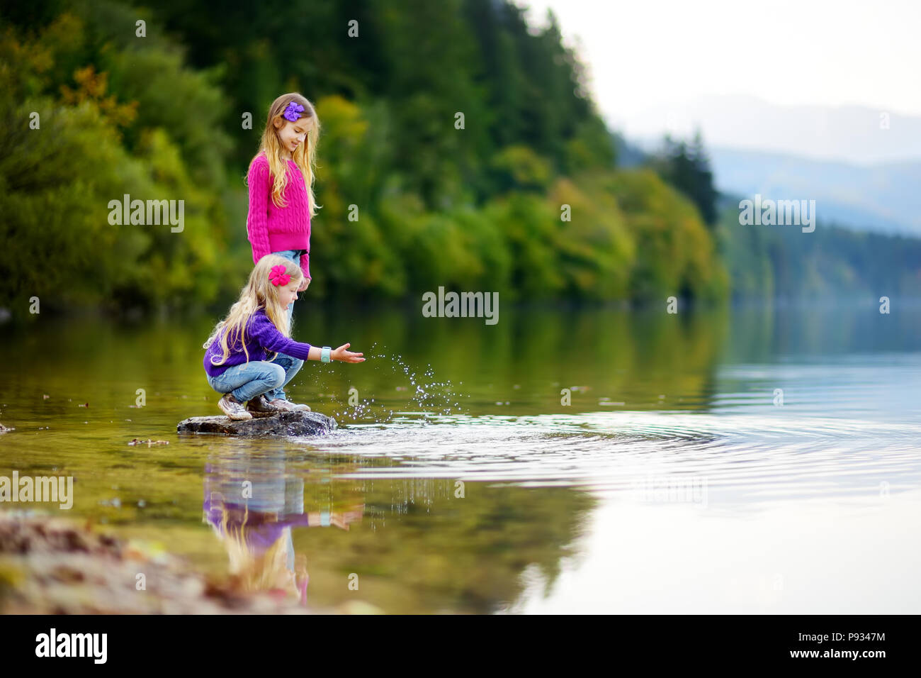 Adorable Schwestern spielen durch Hallstätter See in Österreich an einem warmen Sommertag. Süße Kinder Spaß Spritzwasser und warfen Steine in die Stockfoto