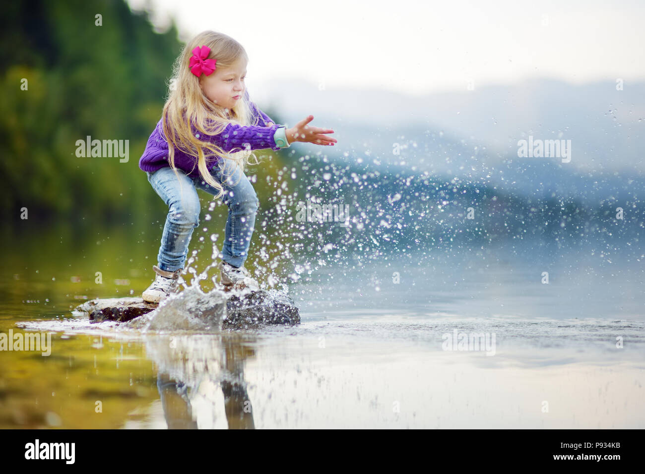 Adorable girl Spielen durch Hallstätter See in Österreich an einem warmen Sommertag. Niedliche Kind Spaß Spritzwasser und warfen Steine in den See. Stockfoto