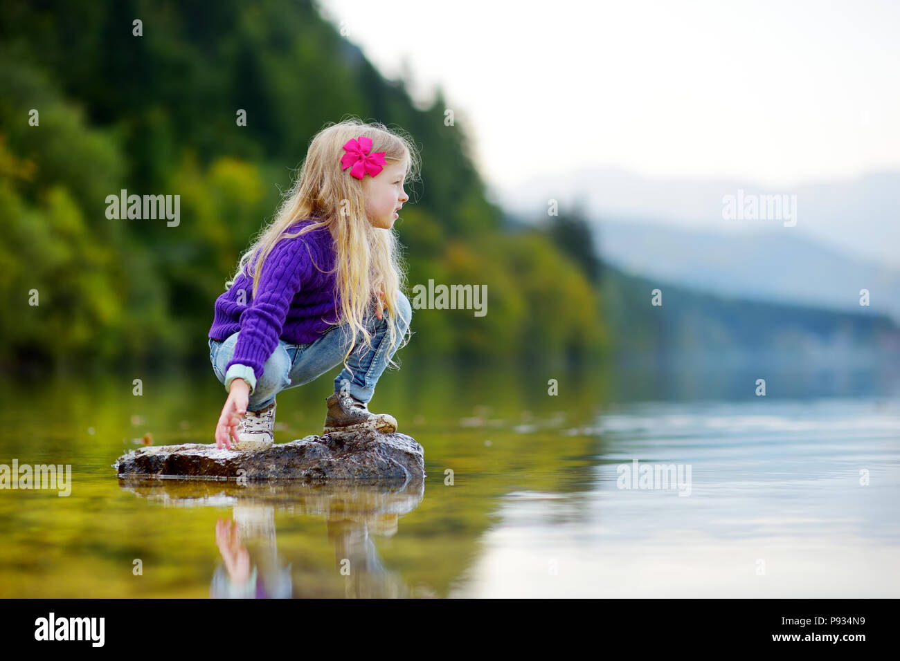 Adorable girl Spielen durch Hallstätter See in Österreich an einem warmen Sommertag. Niedliche Kind Spaß Spritzwasser und warfen Steine in den See. Stockfoto