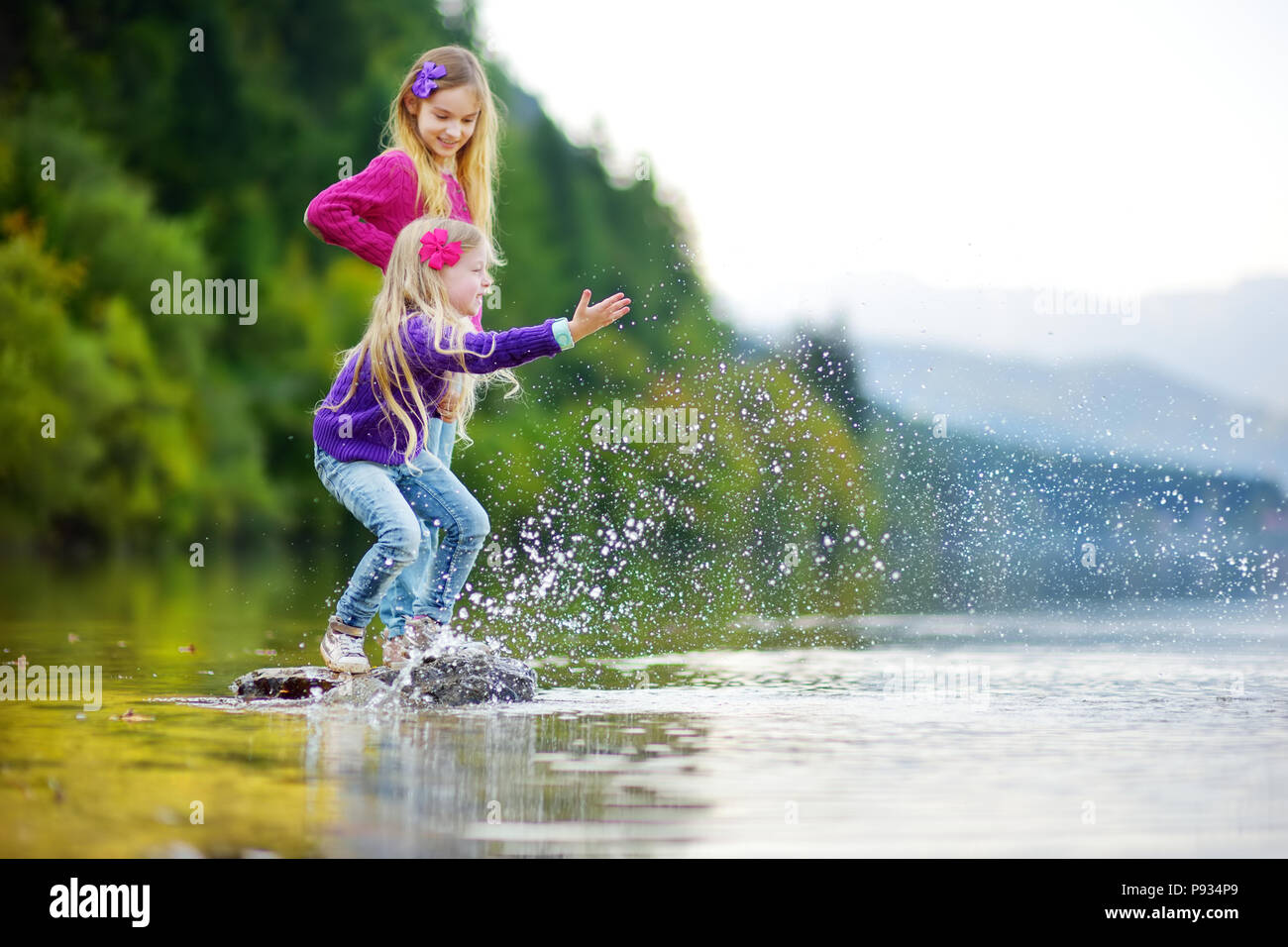 Adorable Schwestern spielen durch Hallstätter See in Österreich an einem warmen Sommertag. Süße Kinder Spaß Spritzwasser und warfen Steine in die Stockfoto