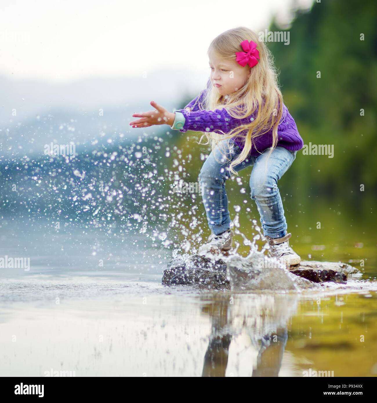 Adorable girl Spielen durch Hallstätter See in Österreich an einem warmen Sommertag. Niedliche Kind Spaß Spritzwasser und warfen Steine in den See. Stockfoto