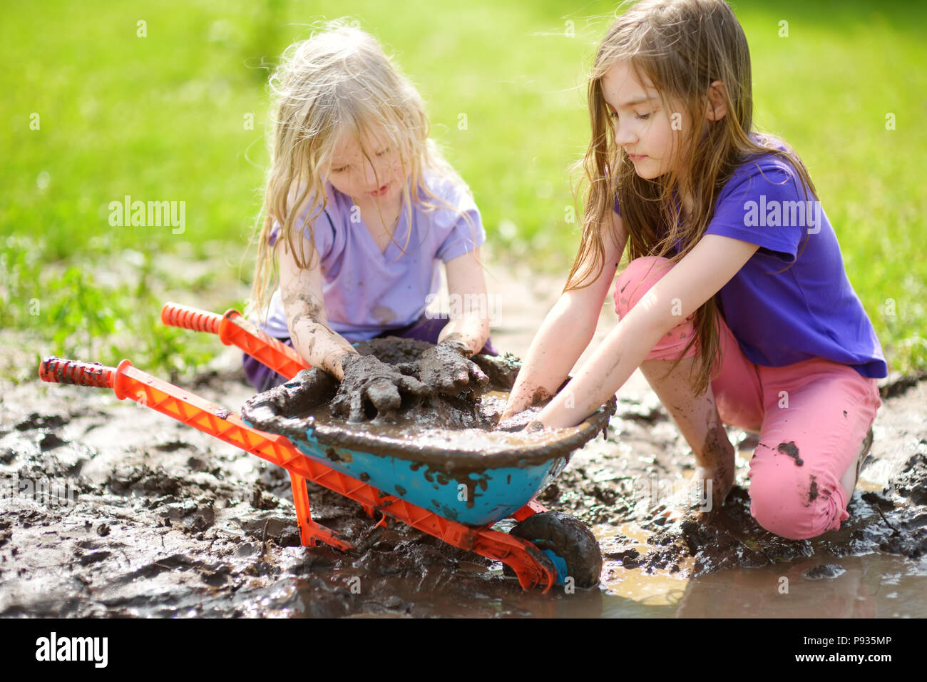 Zwei lustige kleine Mädchen, die in einem großen feuchten Schlamm Pfütze auf sonnigen Sommertag. Kinder Verschmutzung beim Graben in den schlammigen Boden. Unordentliche Spiele im Freien Stockfoto