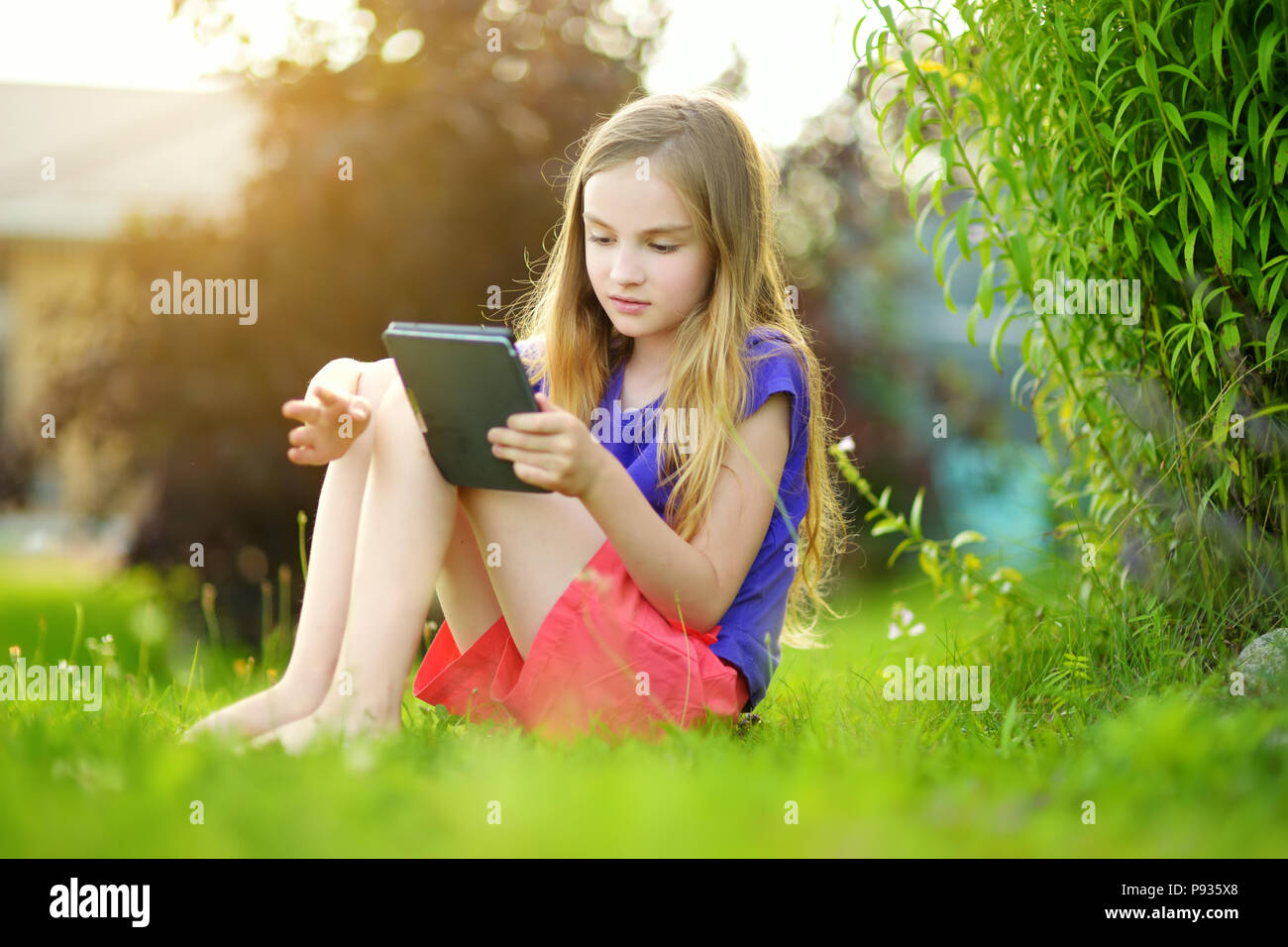 Süße kleine Mädchen sitzt in einem Garten und Lesen ein ebook auf sonnigen Sommerabend. Bildung für Kinder. Stockfoto