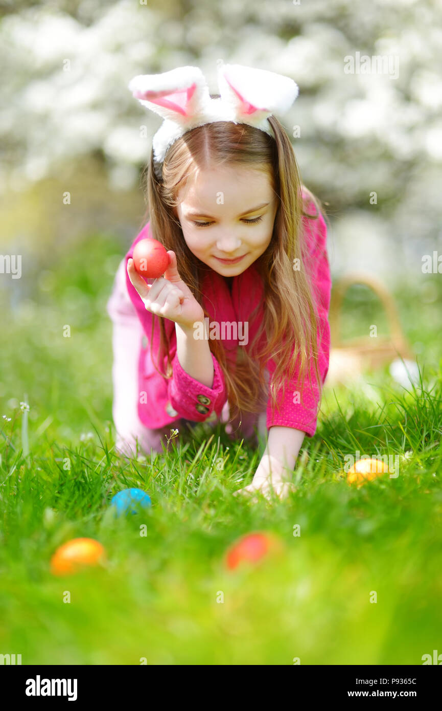 Adorable kleinen Mädchen auf der Jagd nach Osterei in blühende Frühling Garten am Ostersonntag. Niedliche kind Ostern feiern im Freien. Stockfoto