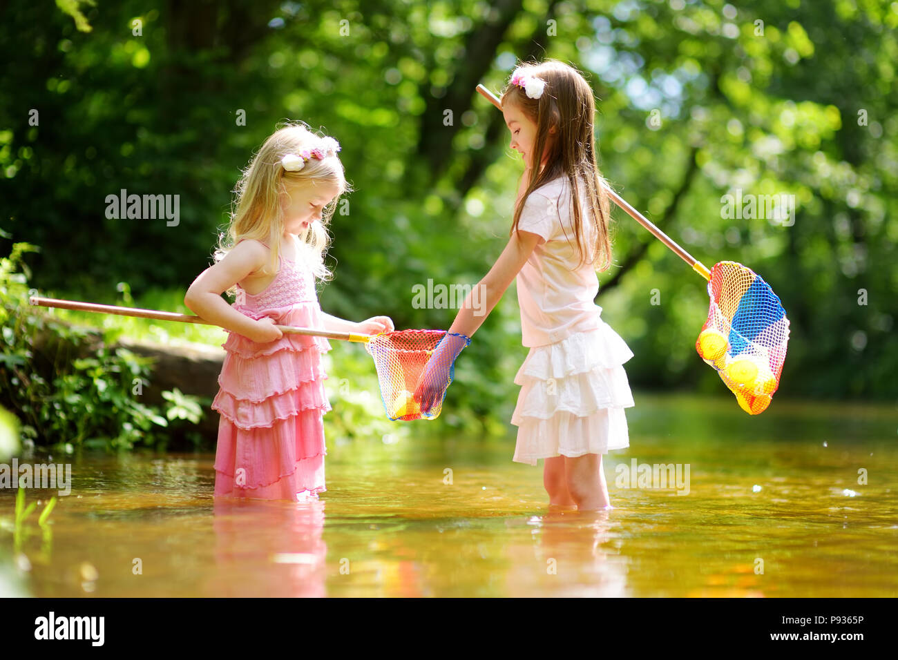 Zwei süße kleine Schwestern spielen in einem Fluss fang Gummienten mit ihren Scoop - Netze an warmen und sonnigen Sommer. Aktiv Sommer Freizeitaktivitäten für Kinder. Stockfoto