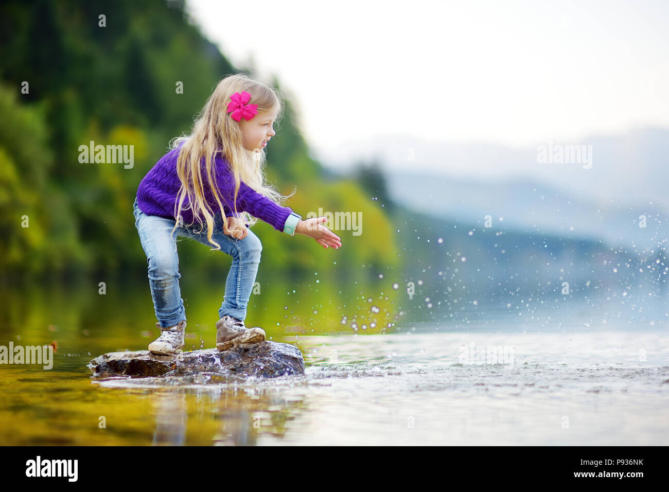 Adorable girl Spielen durch Hallstätter See in Österreich an einem warmen Sommertag. Niedliche Kind Spaß Spritzwasser und warfen Steine in den See. Stockfoto