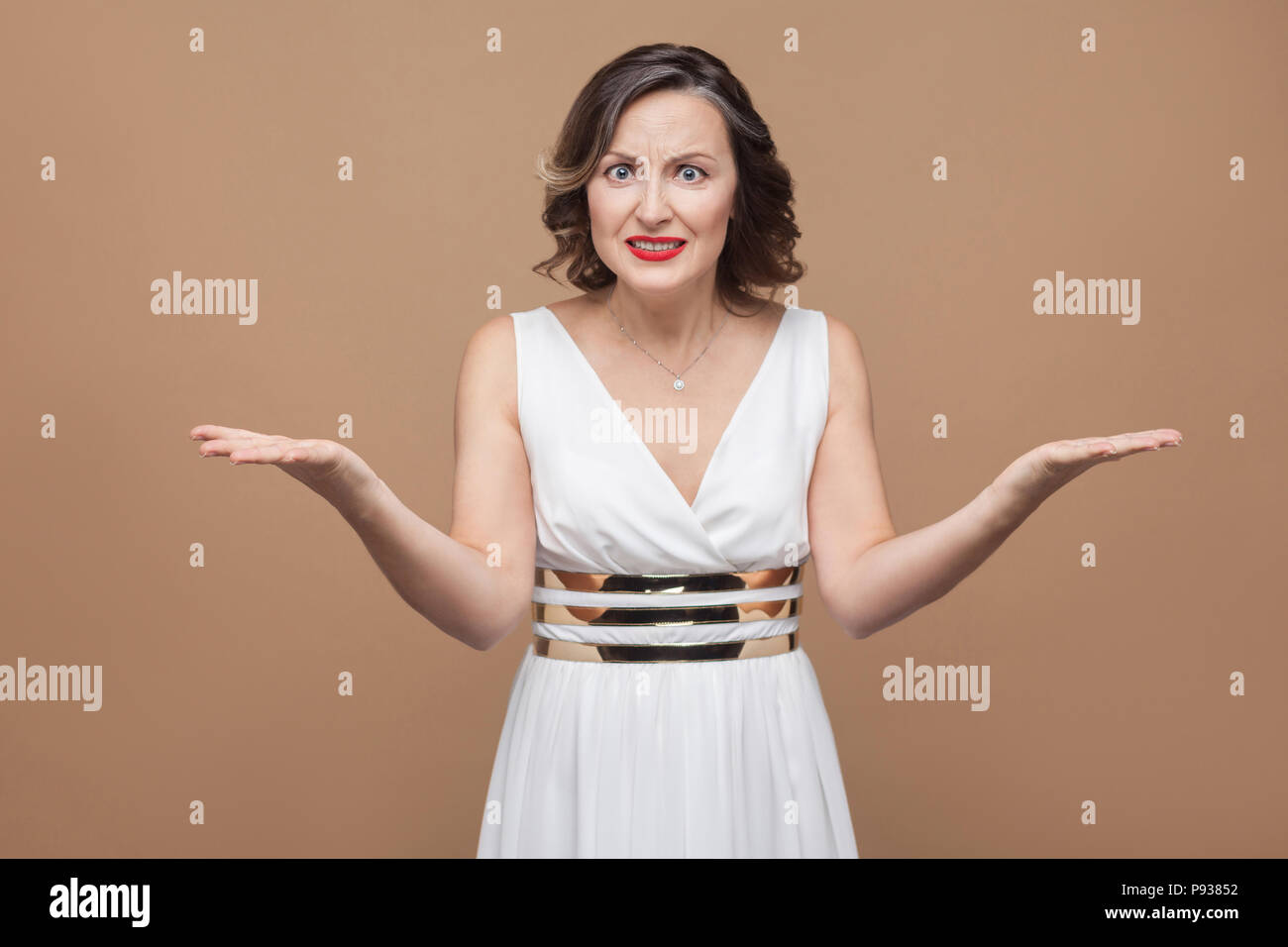 Portrait von Angry im mittleren Alter BOSS Woman bei Kamera schaut. Emotionale Ausdruck Frau im weißen Kleid, roten Lippen und dunkle lockige Frisur. Studio shot, Stockfoto