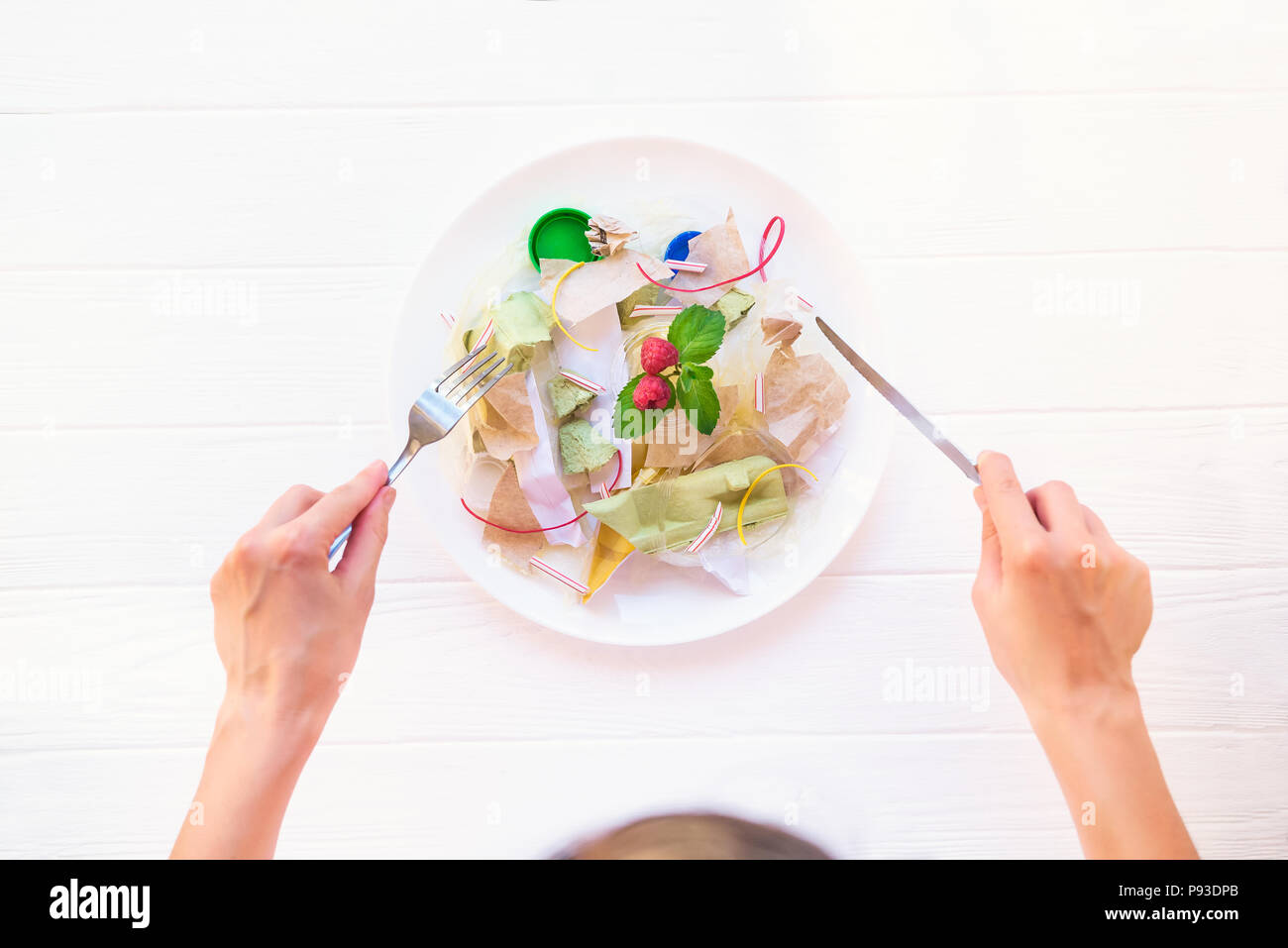 Weibliche Hände, die Messer und Gabel auf der Platte mit unreal Salat aus Recycling von Abfällen, synthetische Inhaltsstoffe. Gvo, E-Nummern. Chemikalien in der Nahrung Stockfoto