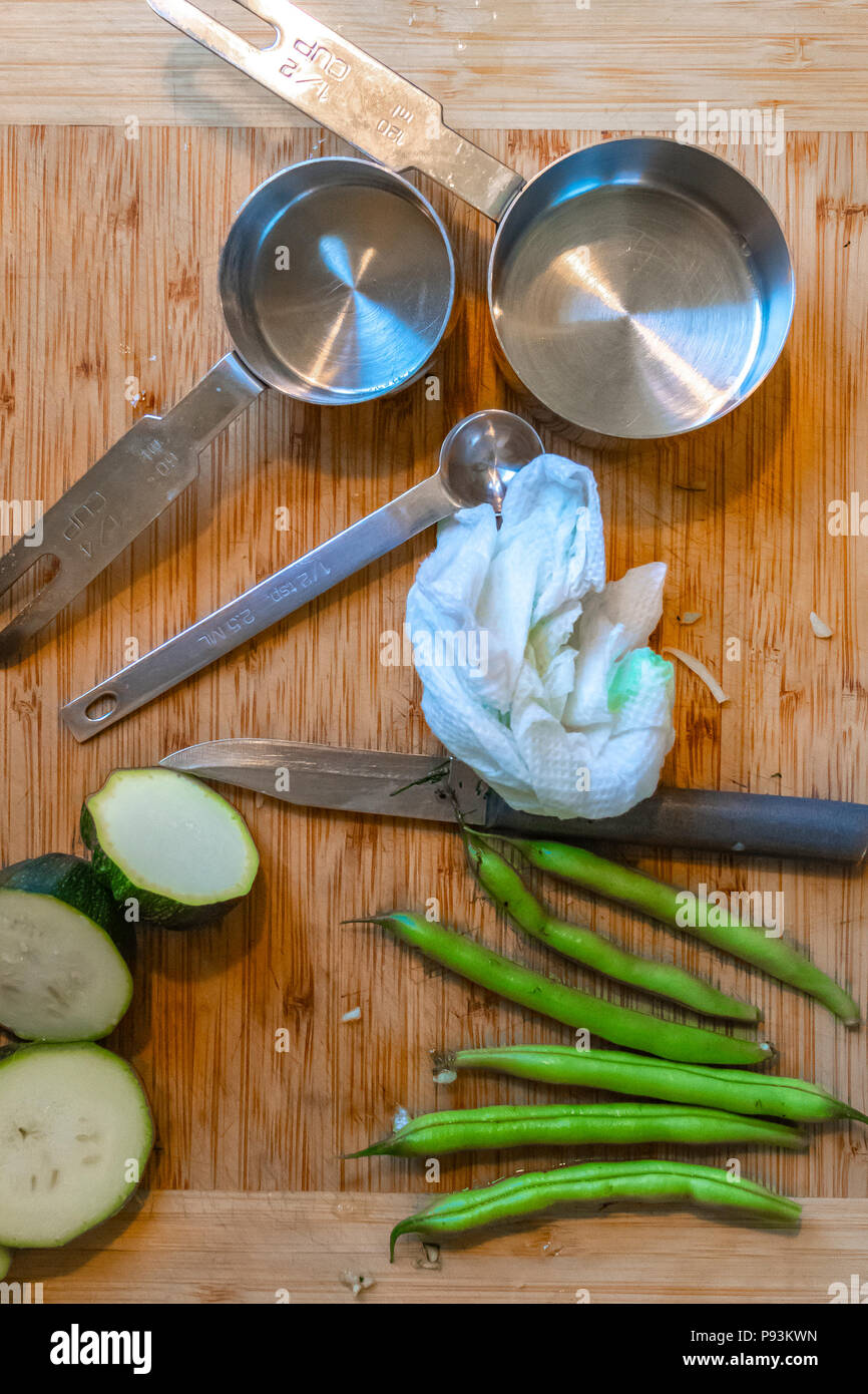 Gurken, grüne Bohnen, messen Utensilien und einem Messer liegen auf einer hölzernen Schneidebrett während der Zubereitung von Speisen. Stockfoto