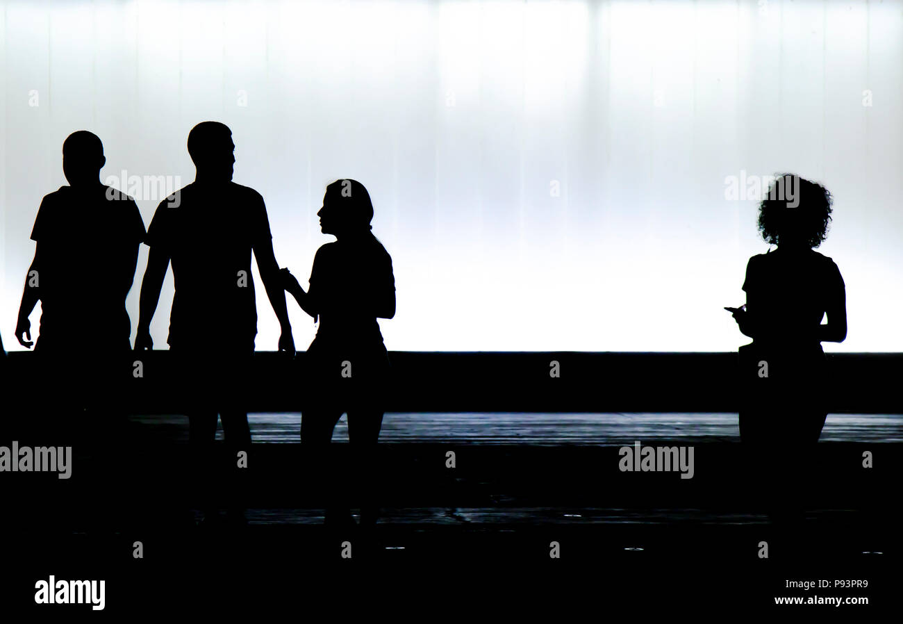 Verschwommene Silhouetten von drei junge Freunde Studenten und ein Junge ist auf der Suche nach einem neuen Mädchen mit lockigem Haar allein stehend in die schwarze und die weiße Nacht Stockfoto