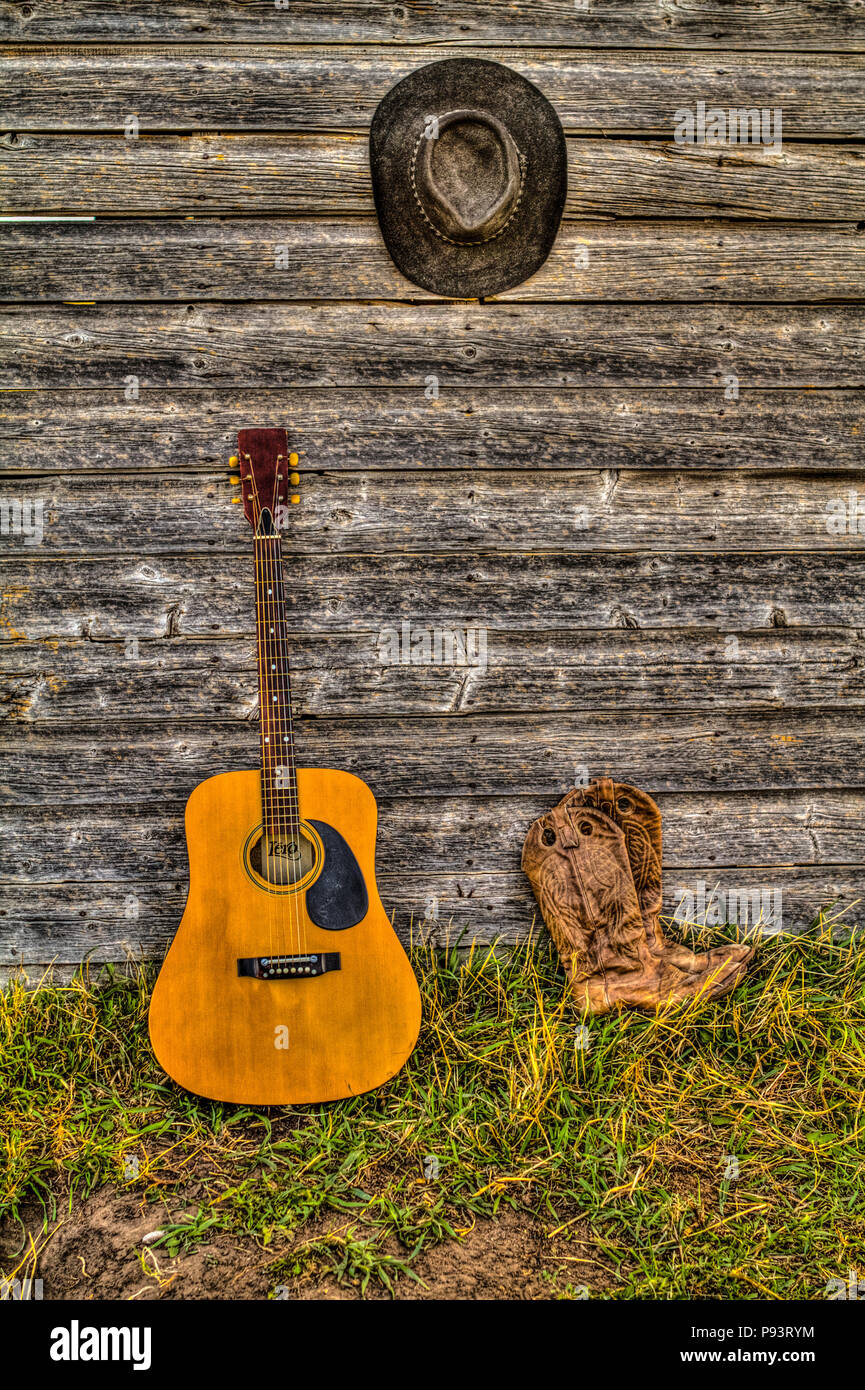 Acoutic Guitar, Cowboy-Hut, Cowboy-Stiefel und alte, Alter Bauernhof Schuppen Wand. Ländlichen Alberta, Kanada. Stockfoto