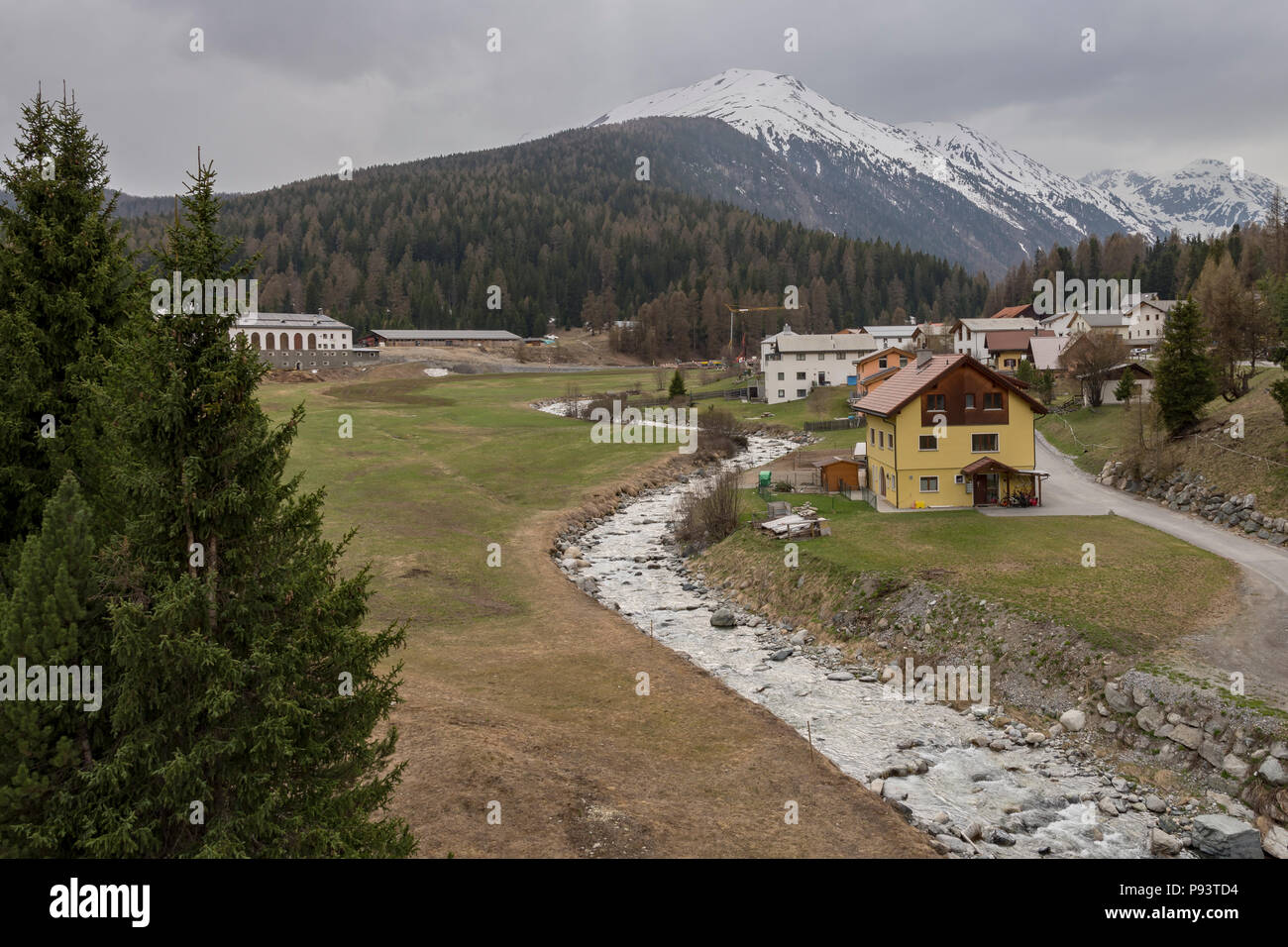 Blick über ein kleines Dorf in der Nähe des Flusses Vallember in der Schweiz mit schneebedeckten Bergen im Hintergrund, Bild von Süden Zernez Schweiz. Stockfoto