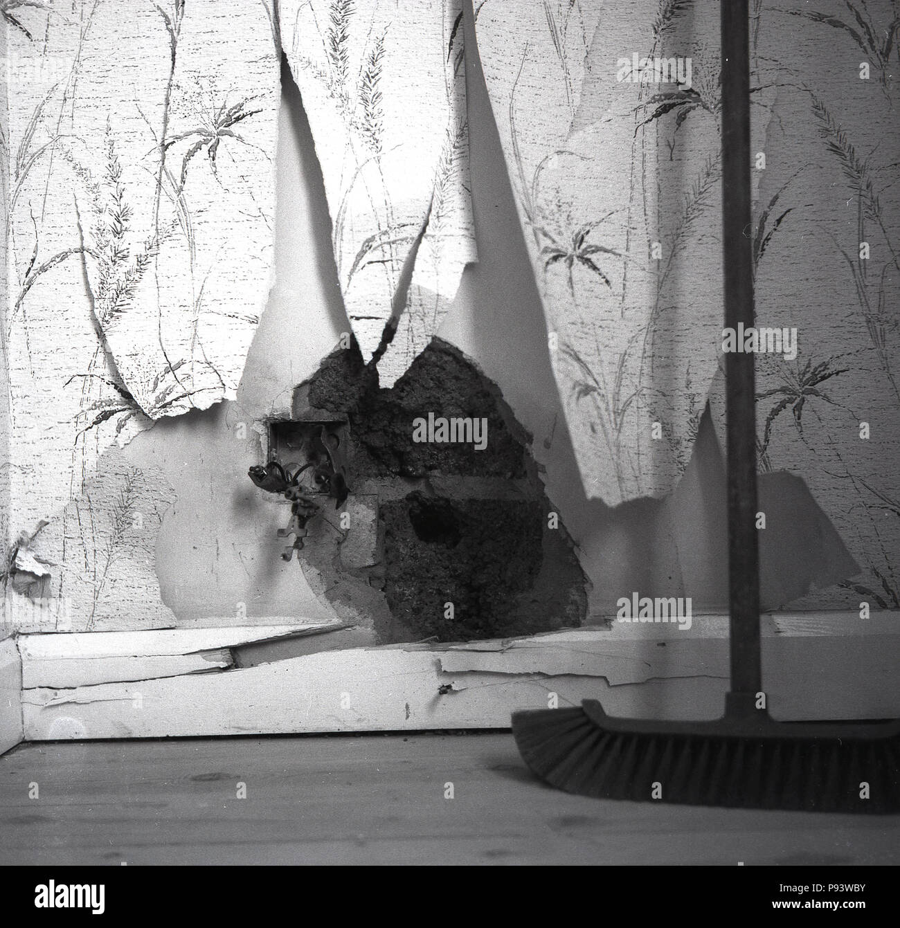 1960, Bild zeigt ein klaffendes Loch in der kaschiervorgänge einer verputzten Wand, zerrissen oder zerfetzte Tapete und Holz- Sockelleisten, die Risse hat sich als Folge von Sturmschäden, England, UK verursacht. Stockfoto