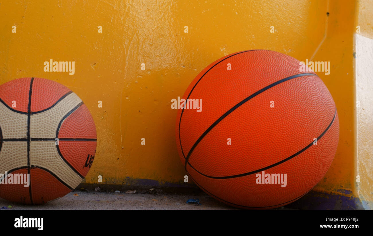 Zwei Basketbälle in verschiedenen Größen unter der gelben Wand liegen Stockfoto