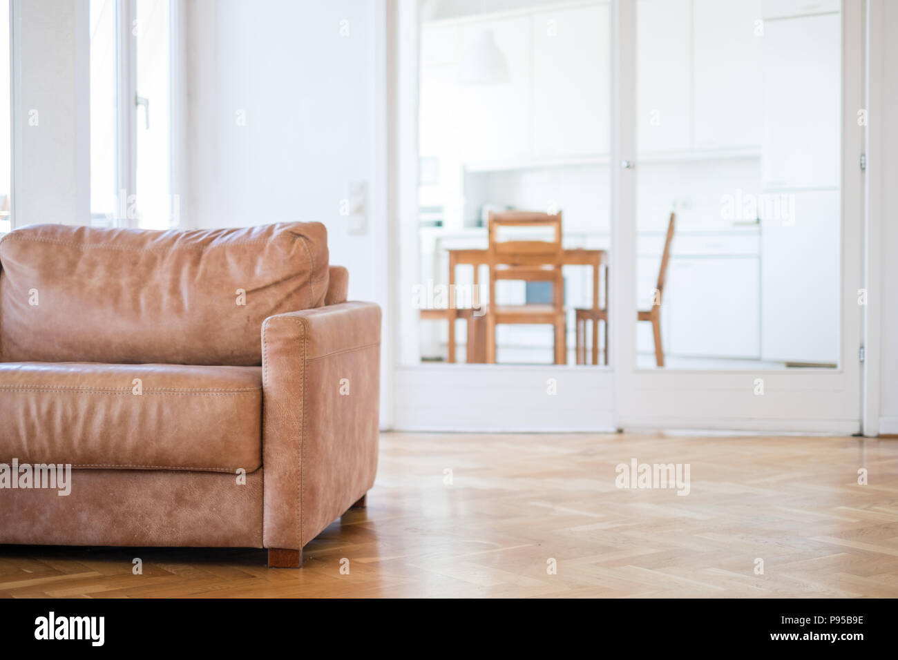 Leere Couch im Wohnzimmer mit Parkettboden, Küche und im Hintergrund - Stockfoto