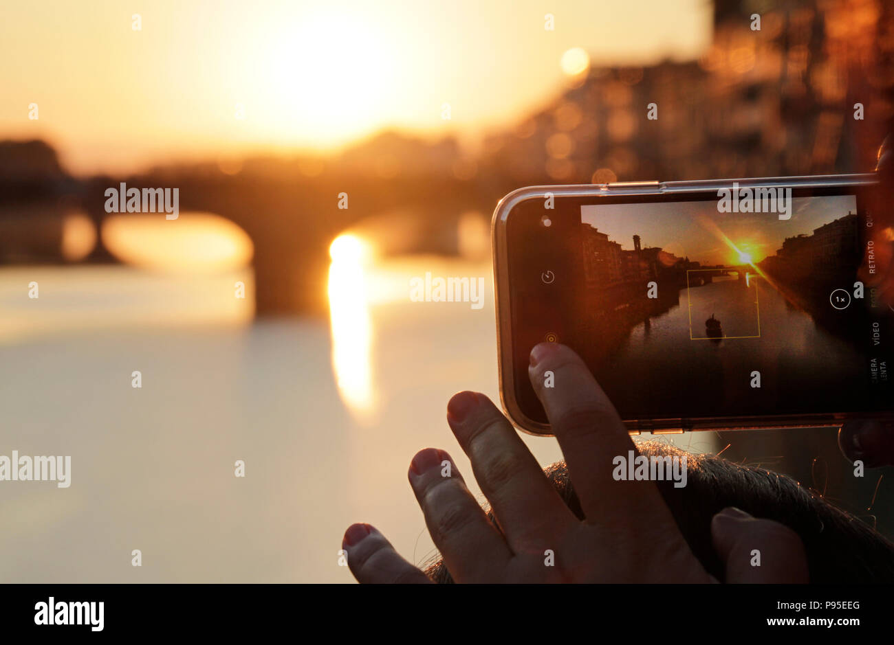 Eine Frau mit Sonnenbrille verwendet Ihr Smartphone ein Foto eines Sonnenuntergangs in Florenz, Italien Stockfoto