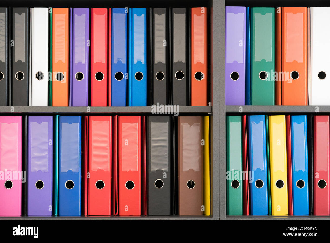 Mehrfarbige A4-Ringordner in Reihen auf einem Bücherregal / Aktenschrank in einem Büro Stockfoto