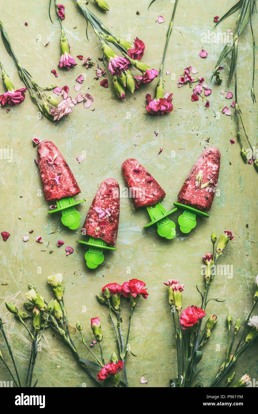 Red hausgemachte Obst und Beeren Eis oder Eis am Stiel auf Teal rustikalen grünen Tisch Hintergrund, mit Garten Blumen, Ansicht von oben eingerichtet. Country Style Stockfoto